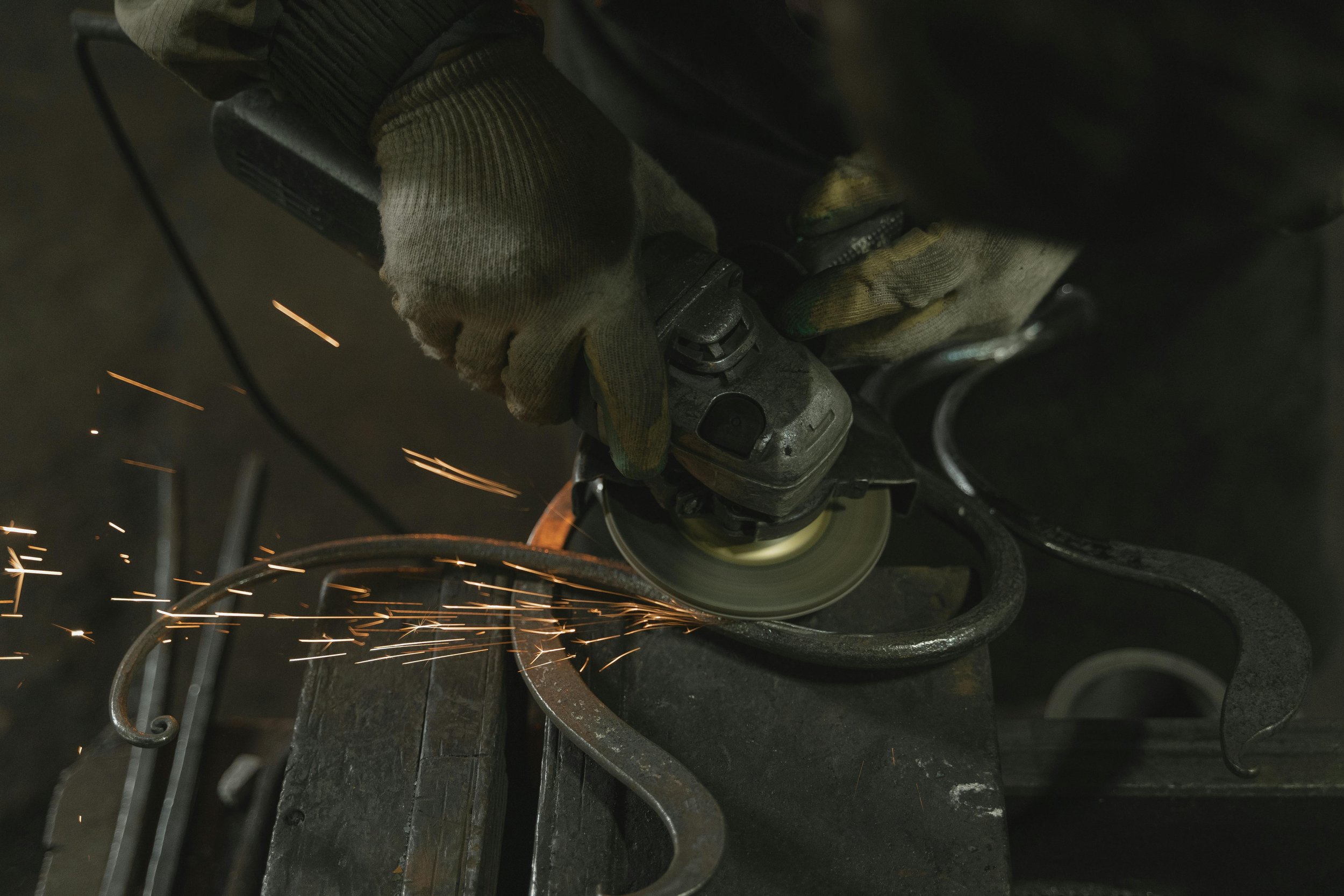 Eine Person trägt Handschuhe und verwendet eine Schleifmaschine, um ein Metallstück zu bearbeiten, wobei Funken fliegen.