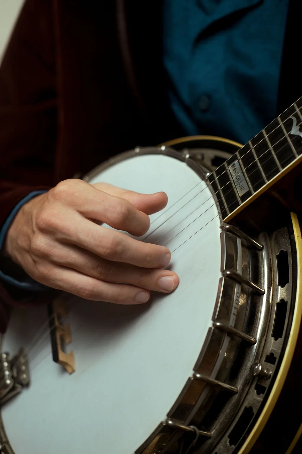 Close-up of a person playing a banjo, focusing on their left hand on the strings and part of the instrument's body.