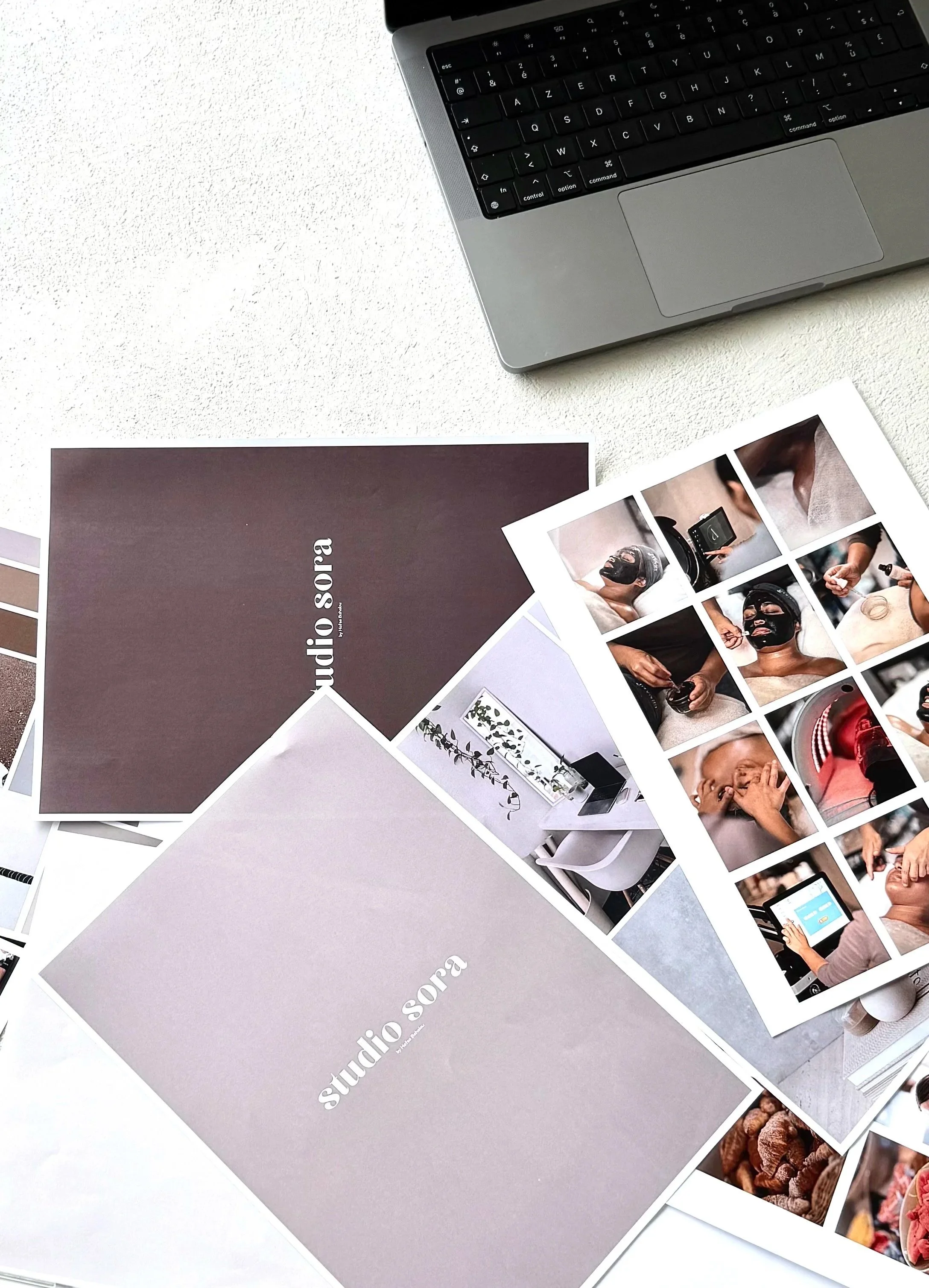 A white desk with a MacBook, several printed photographs, and brochures from Studio Sora, a photography studio.
