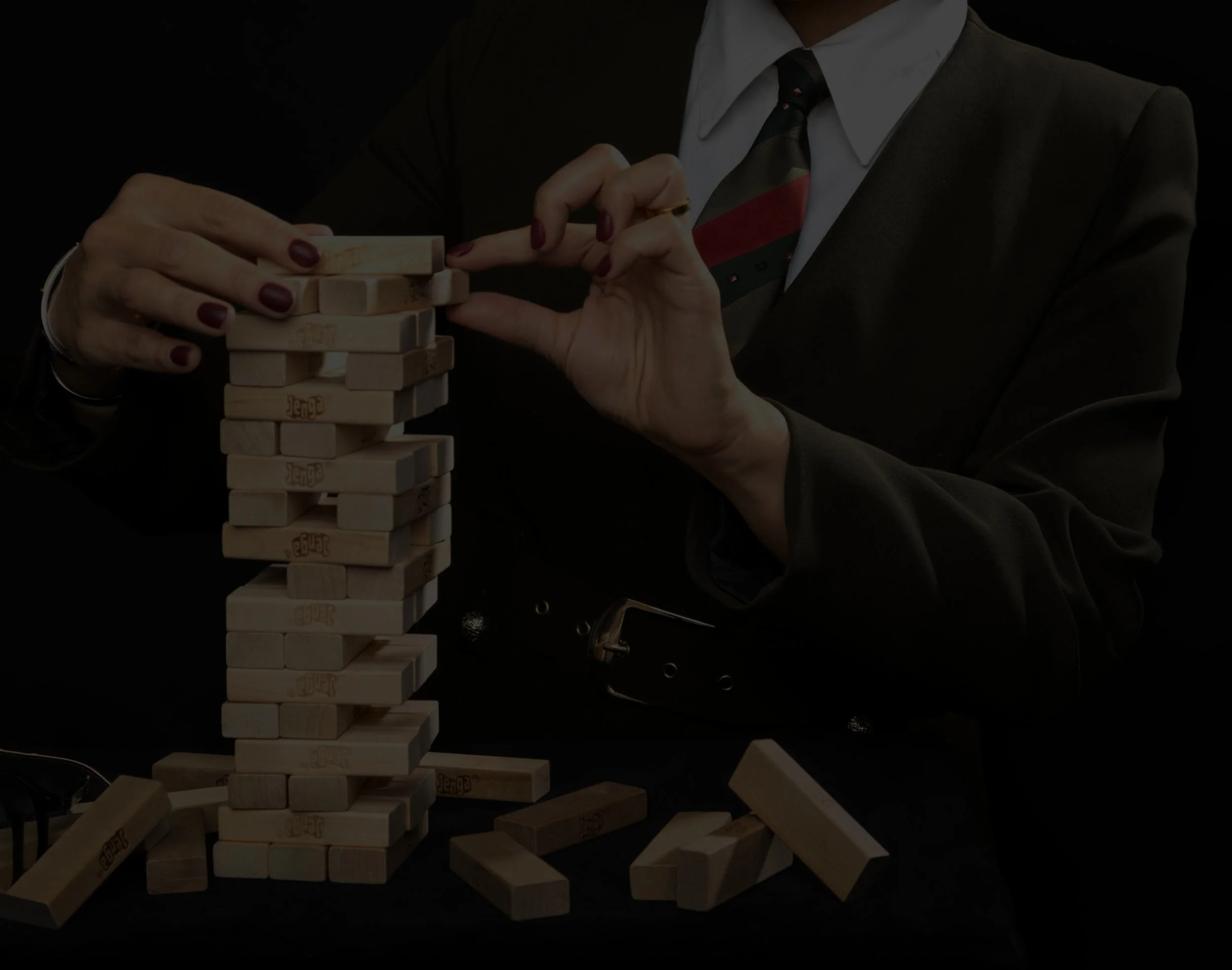 A woman in a business suit and tie playing a giant Jenga game, carefully removing a block from the tower.