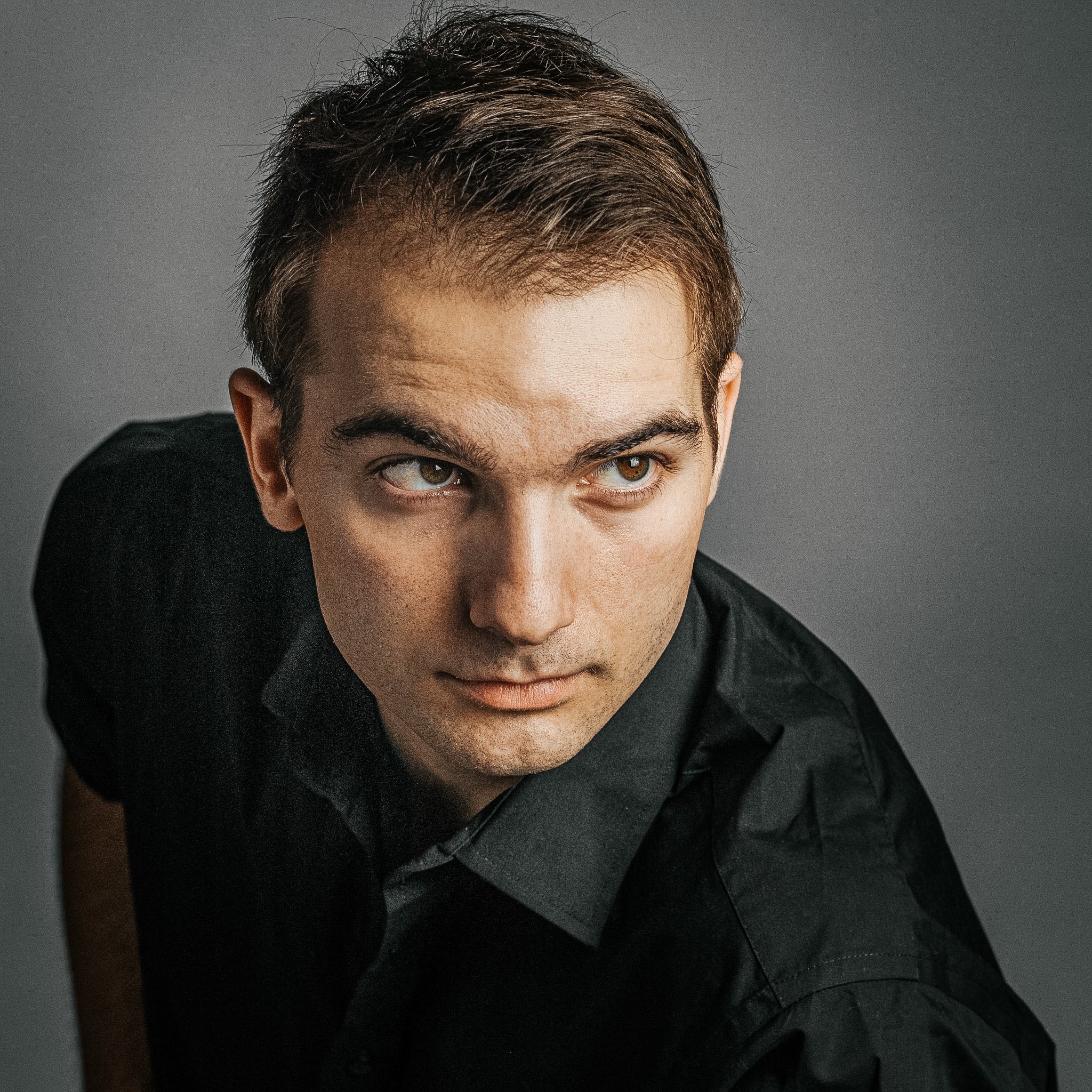 Close-up of a man's face and eyes, with dark hair and a serious expression, against a dark gray background.