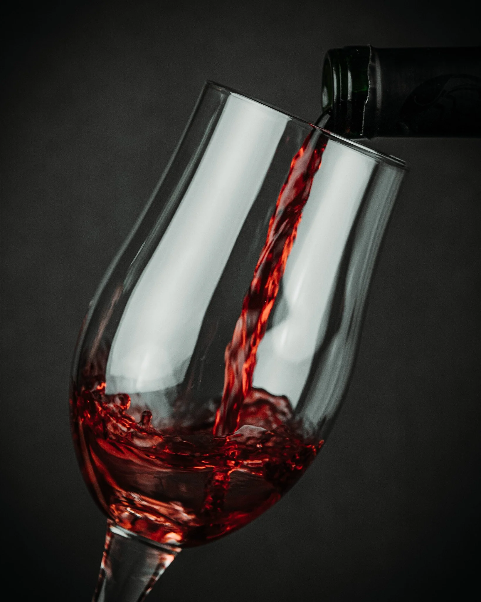 A close-up of red wine being poured into a wine glass against a black background.