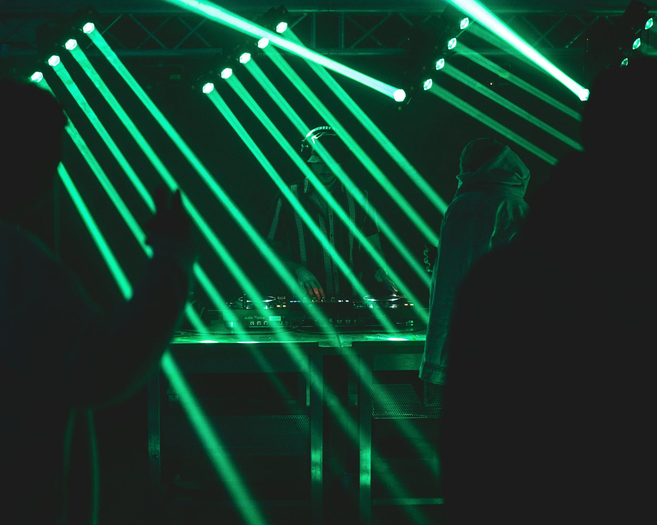 People dancing at a nightclub with bright green laser lights and a DJ performing on stage.