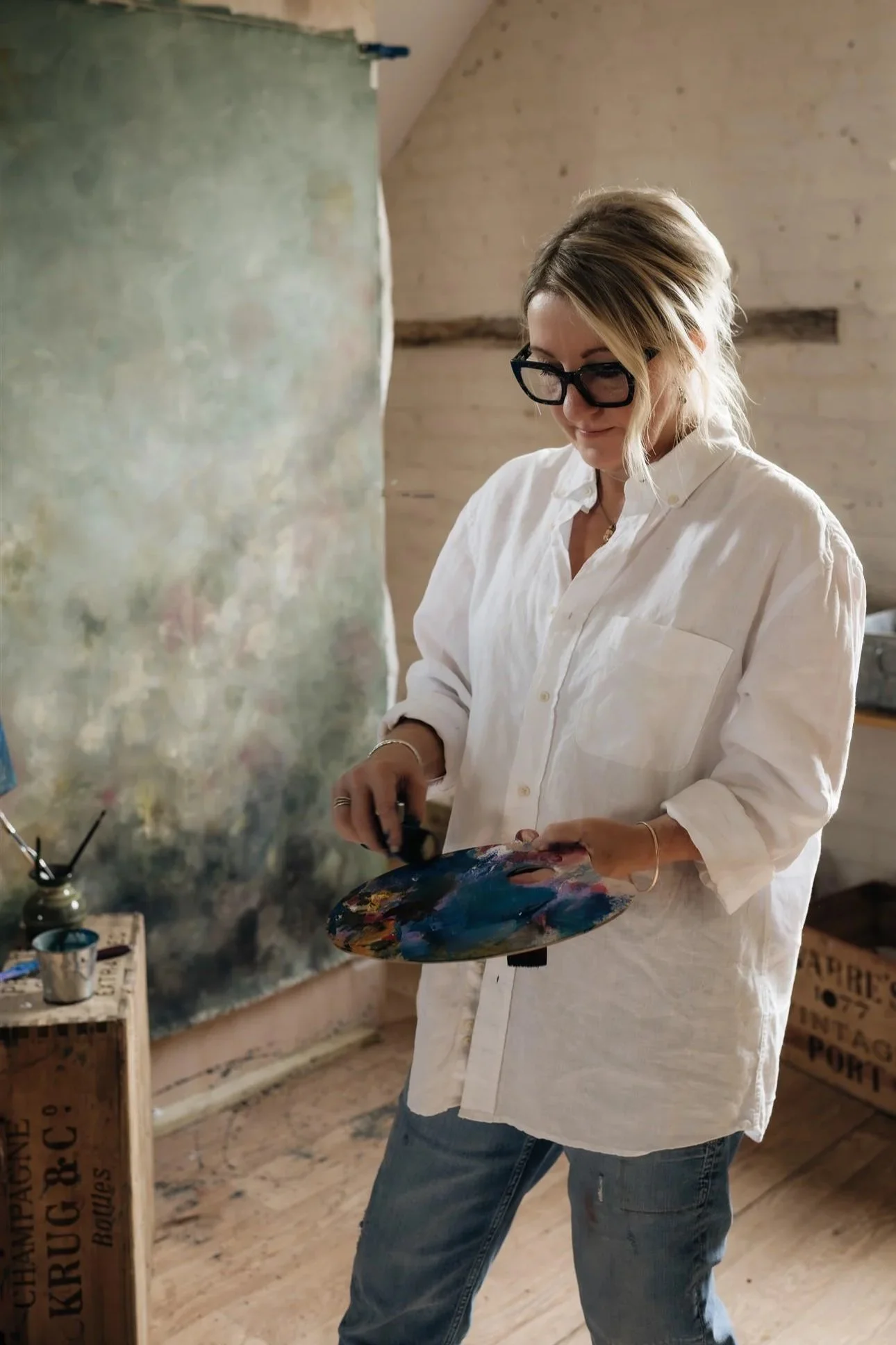 Artist Sarah Pitt holding a paint palette and sponge standing in front of a large green toned canvas