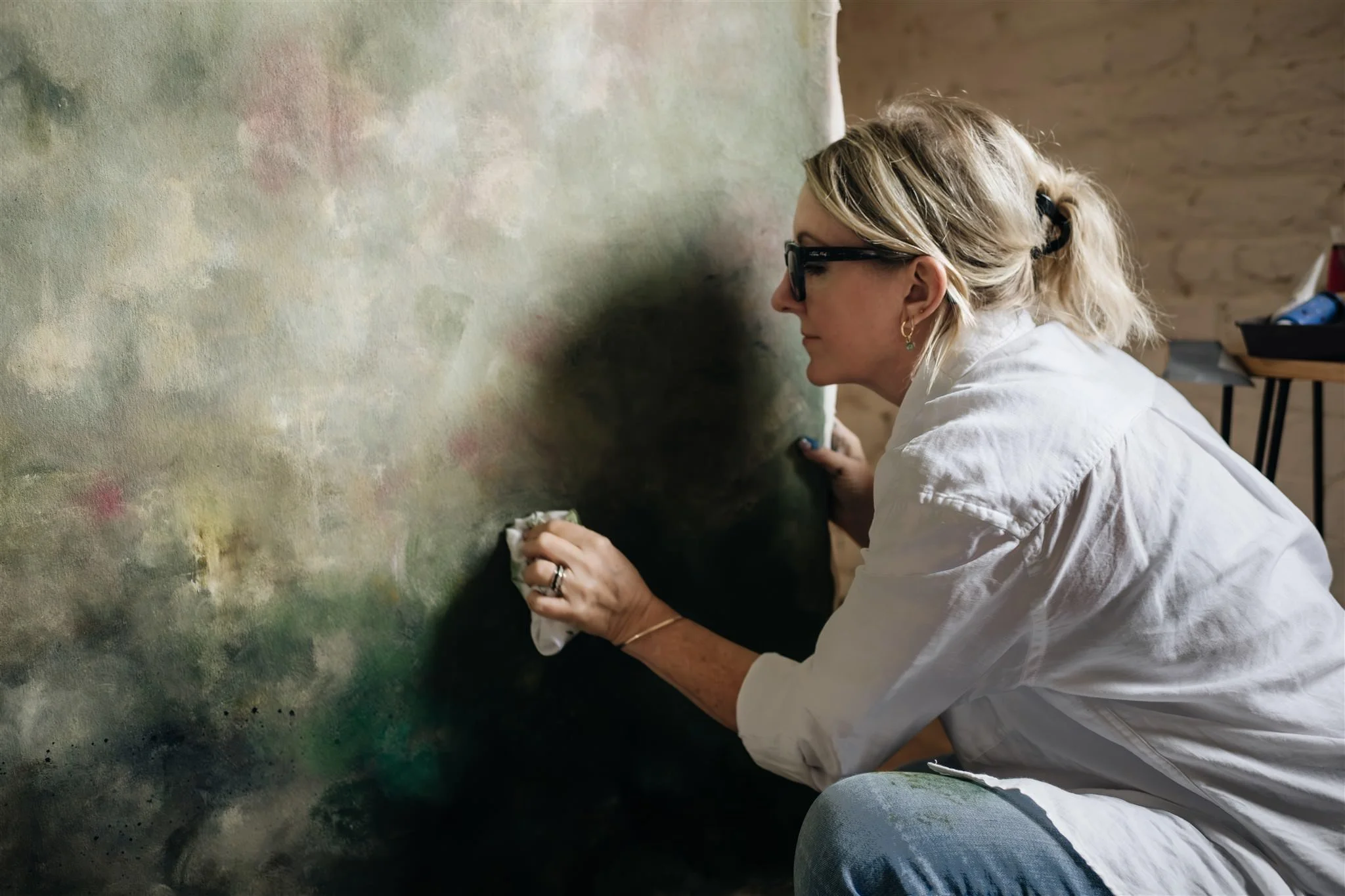 Artist sarah Pitt knelt in front of her canvas artwork touching up her artwork with a fabric rag.