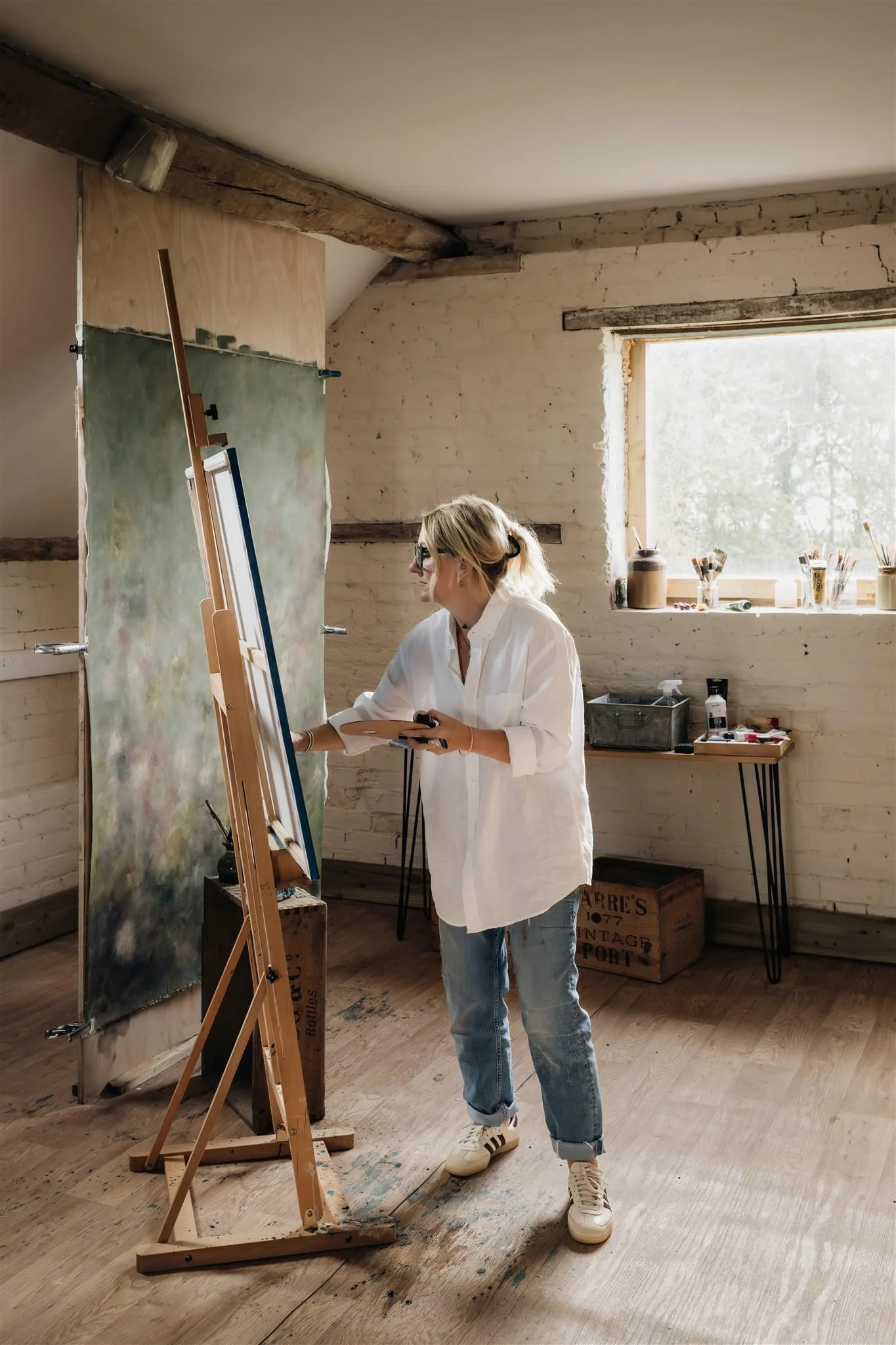 A large canvas being painted in green tones by Sarah Pitt, she is holding her paint palette and paintbrush in her studio