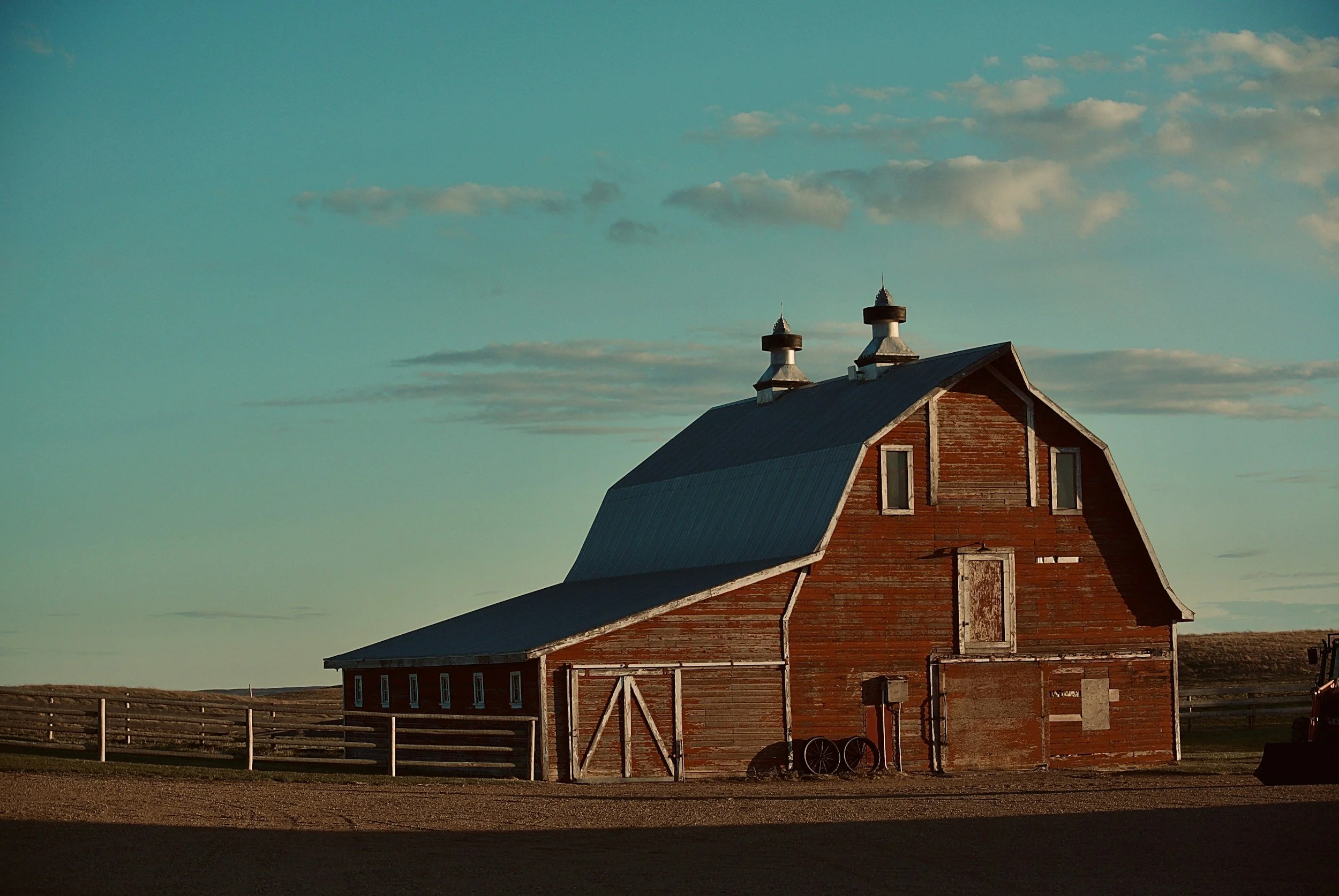Old wooden barn with a metal roof on a rural landscape during sunset.