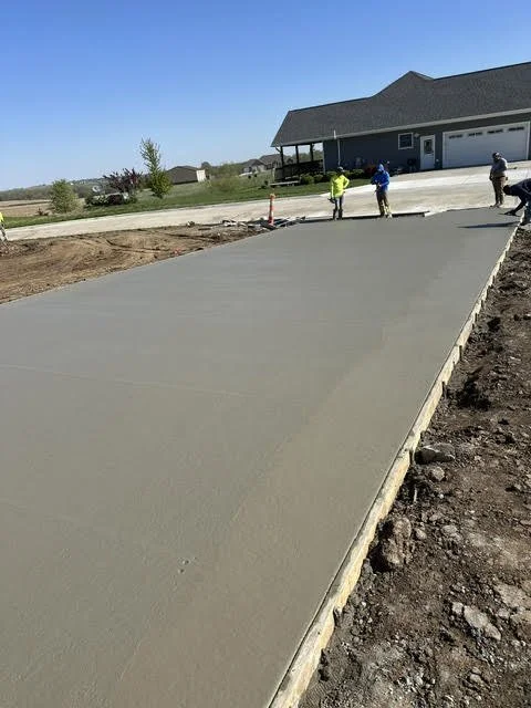 Construction workers are working on a freshly poured concrete driveway in front of a house.
