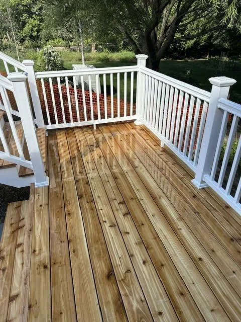 Wooden deck with white railing overlooking a yard with trees and grass.