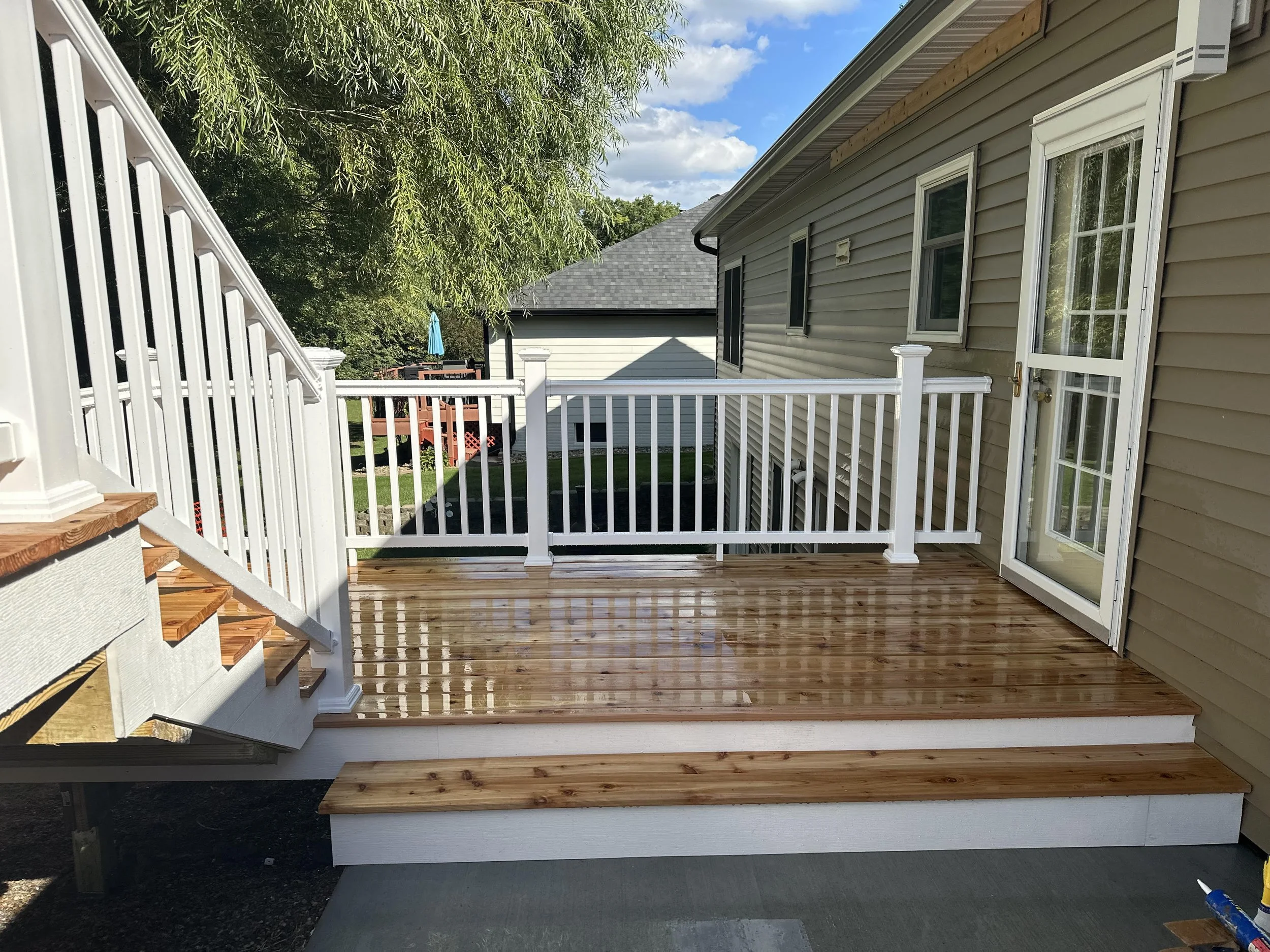 Newly installed wooden deck with white railing outside a beige house with a glass sliding door.