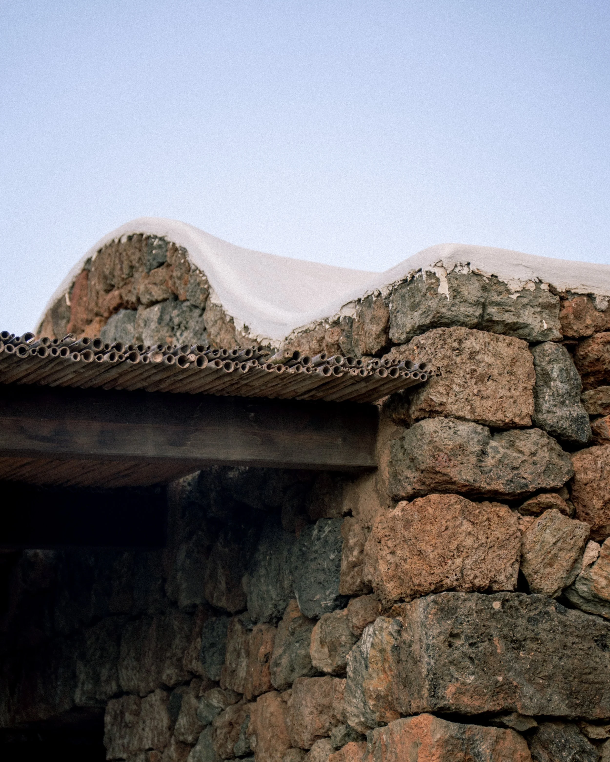 Foto di un tetto in pietra con un muretto di pietra e una copertura di canne di legno, con il cielo azzurro sullo sfondo.