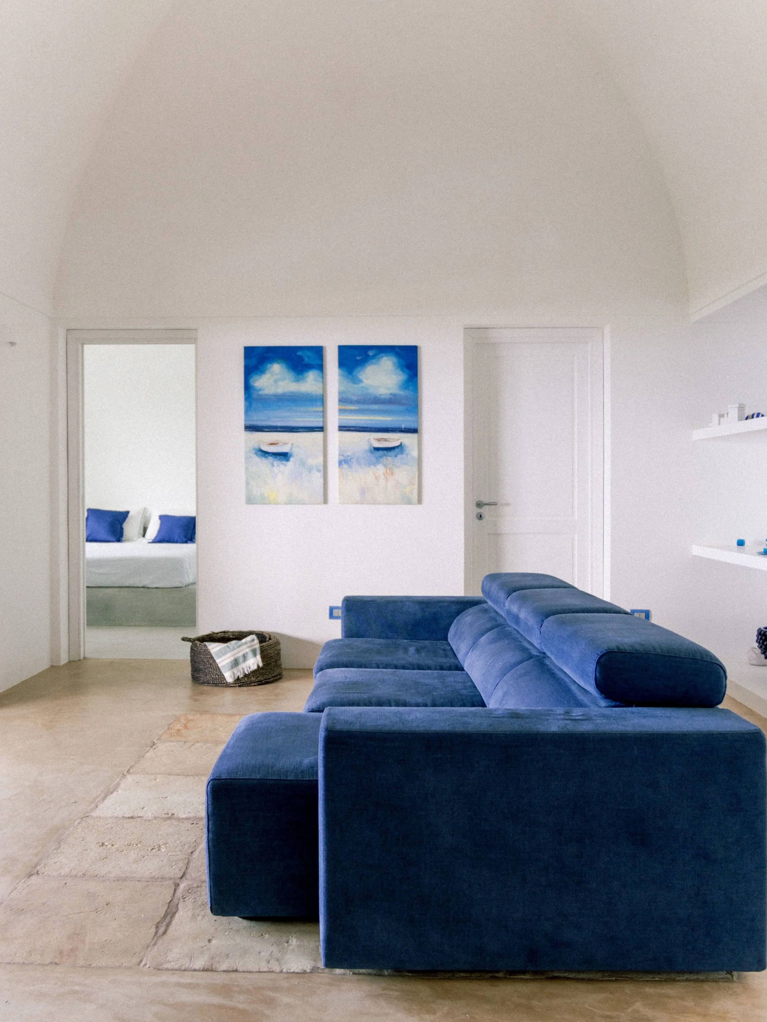 Soggiorno vista mare con divano blu e pareti bianche.