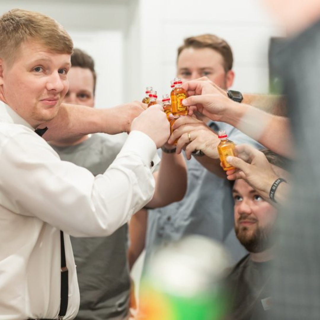 A group of men raising small bottles of alcohol together in a toast, celebrating and smiling.