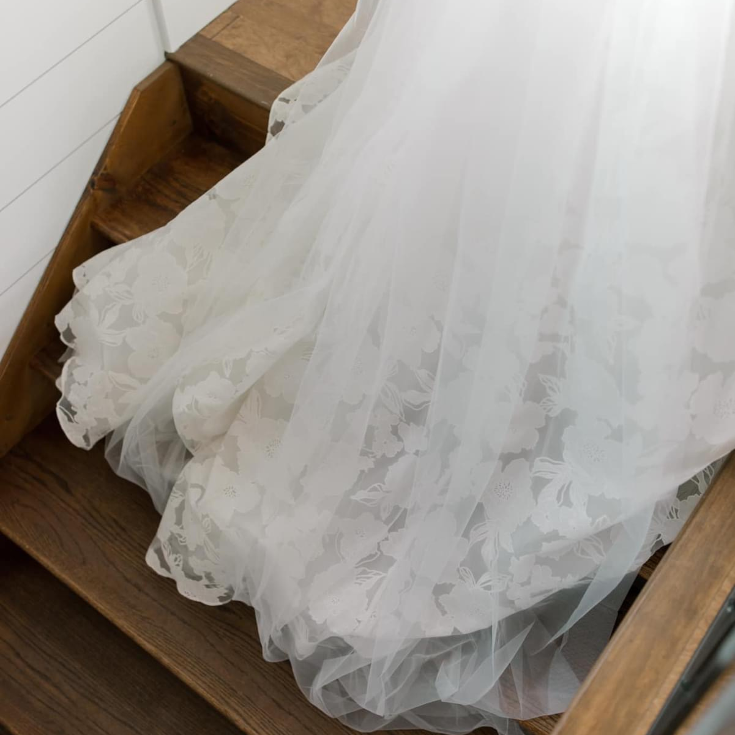 A wooden stair with a white lace curtain with floral patterns draped over it.