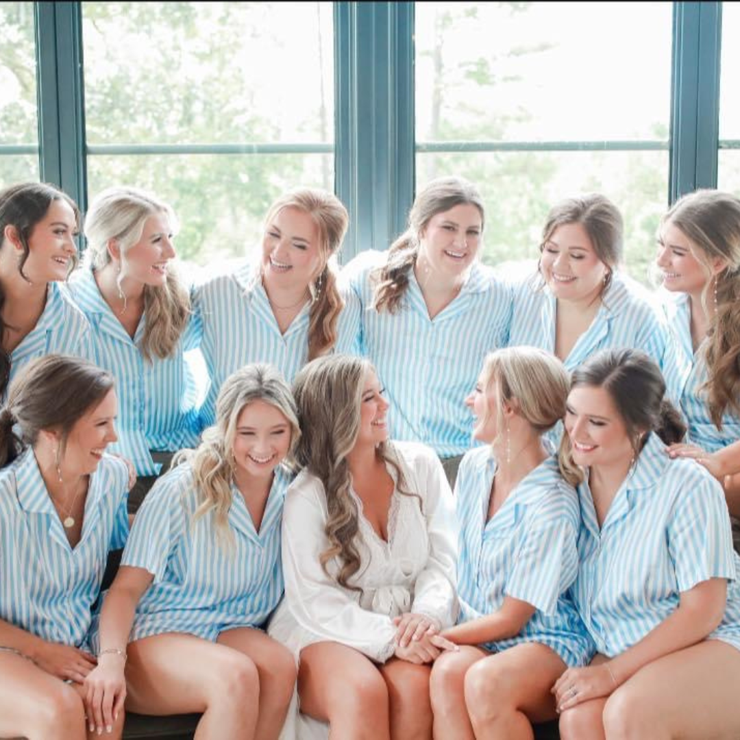 A large group of women, mostly wearing matching blue and white striped pajamas, sitting on a couch, laughing, and enjoying each other's company.