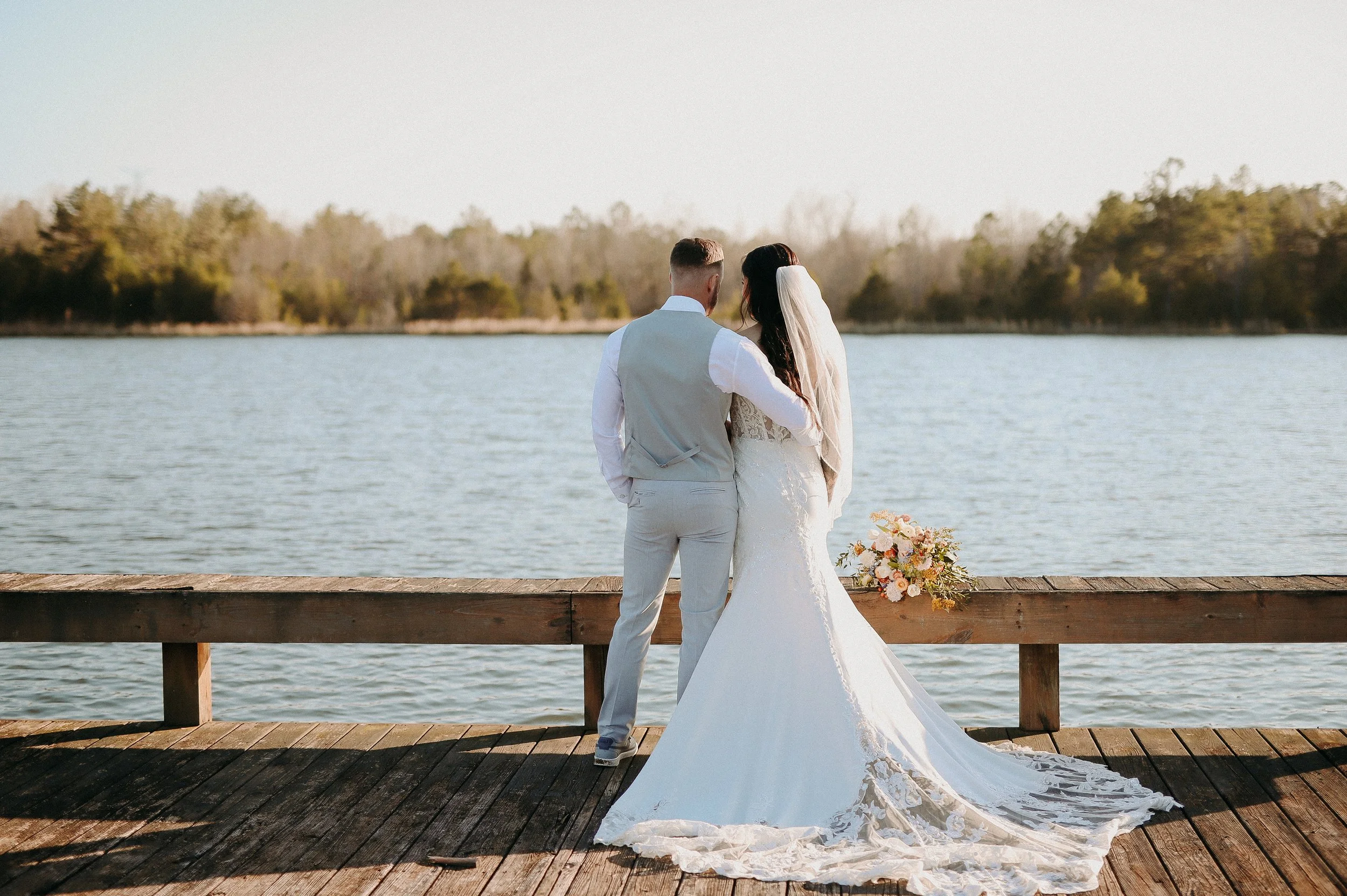 A bride and groom standing on a wooden dock overlooking a body of water during their wedding.
