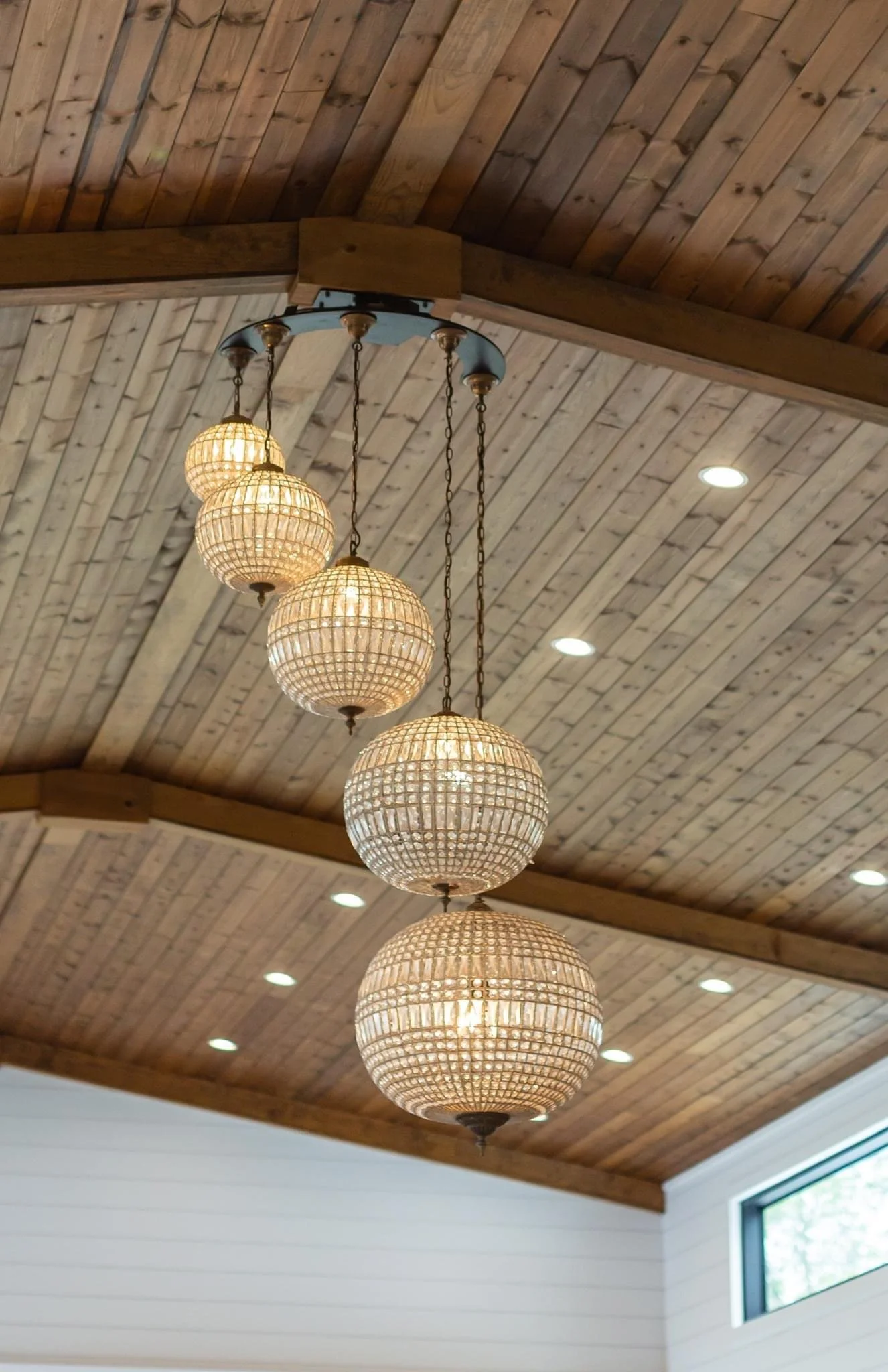 A chandelier with five spherical rattan lamps hanging from a wooden ceiling in a room.