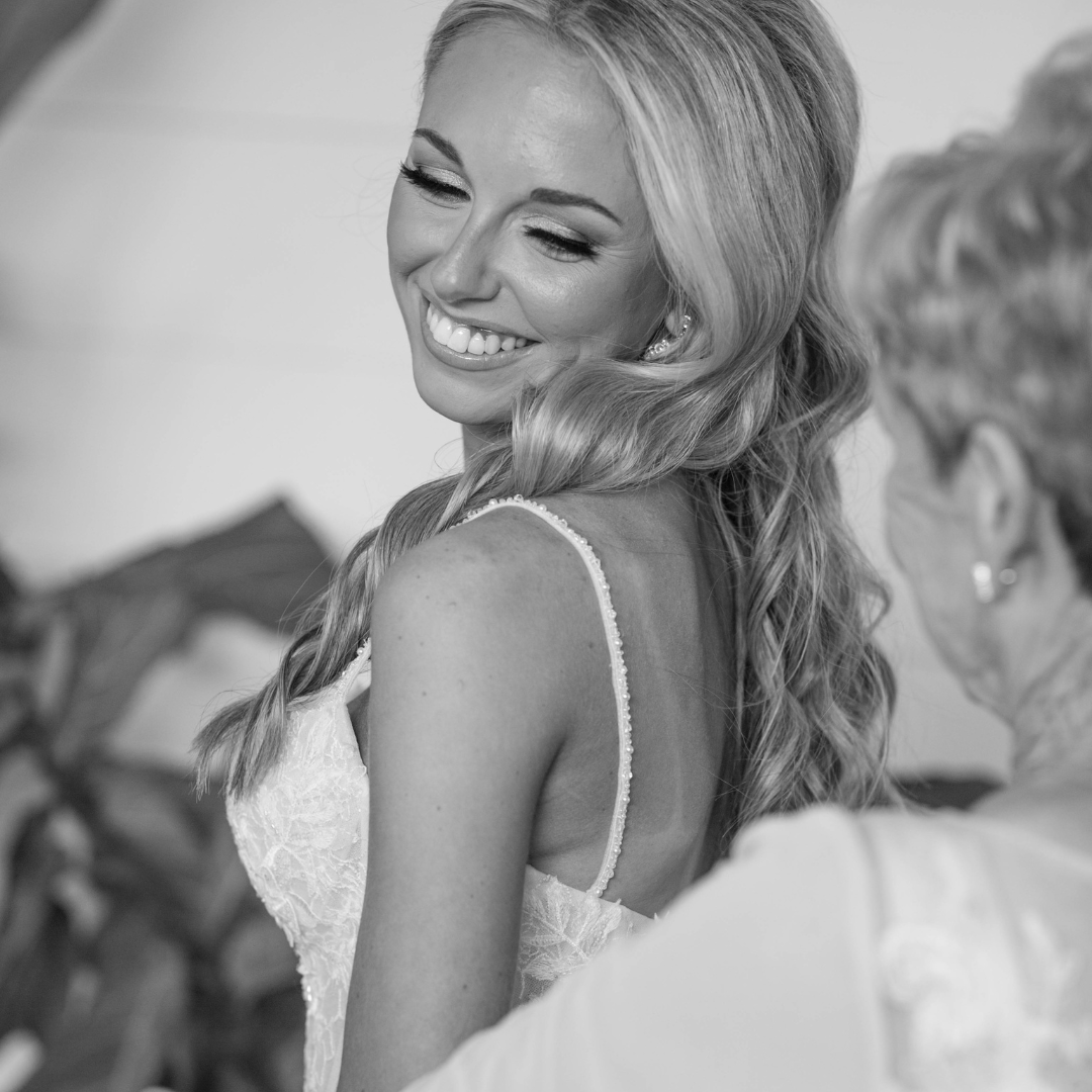 A smiling blonde woman in a wedding dress looking over her shoulder.