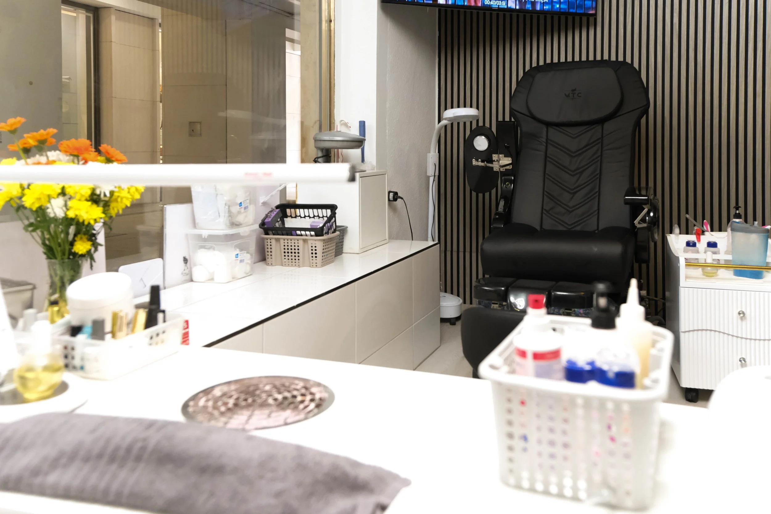Ein Arzt- oder Apothekenraum mit medizinischen Utensilien, einer Behandlungsliege, einer Vase mit gelben und orangenen Blumen, und verschiedenen medizinischen Gegenständen auf Theken. Es gibt auch einen Sitzbereich und Geräte für medizinische Untersu