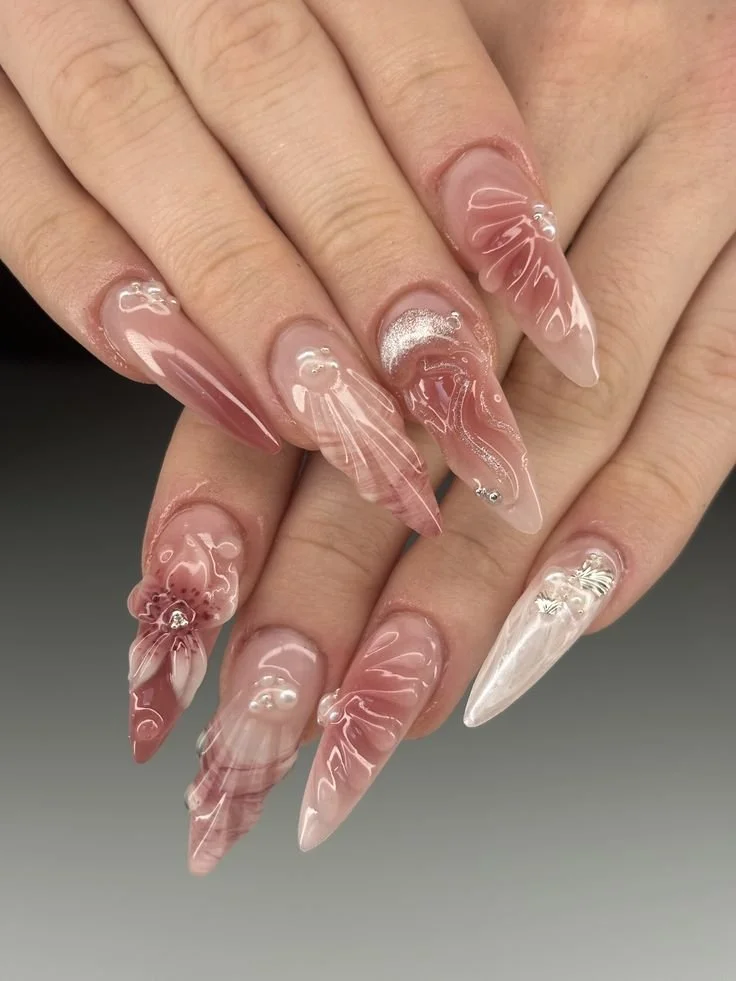 Nahaufnahme von künstlichen Nägeln mit pinkfarbener, transparenter und mit Perlen und Designs verzierten Nagellack
