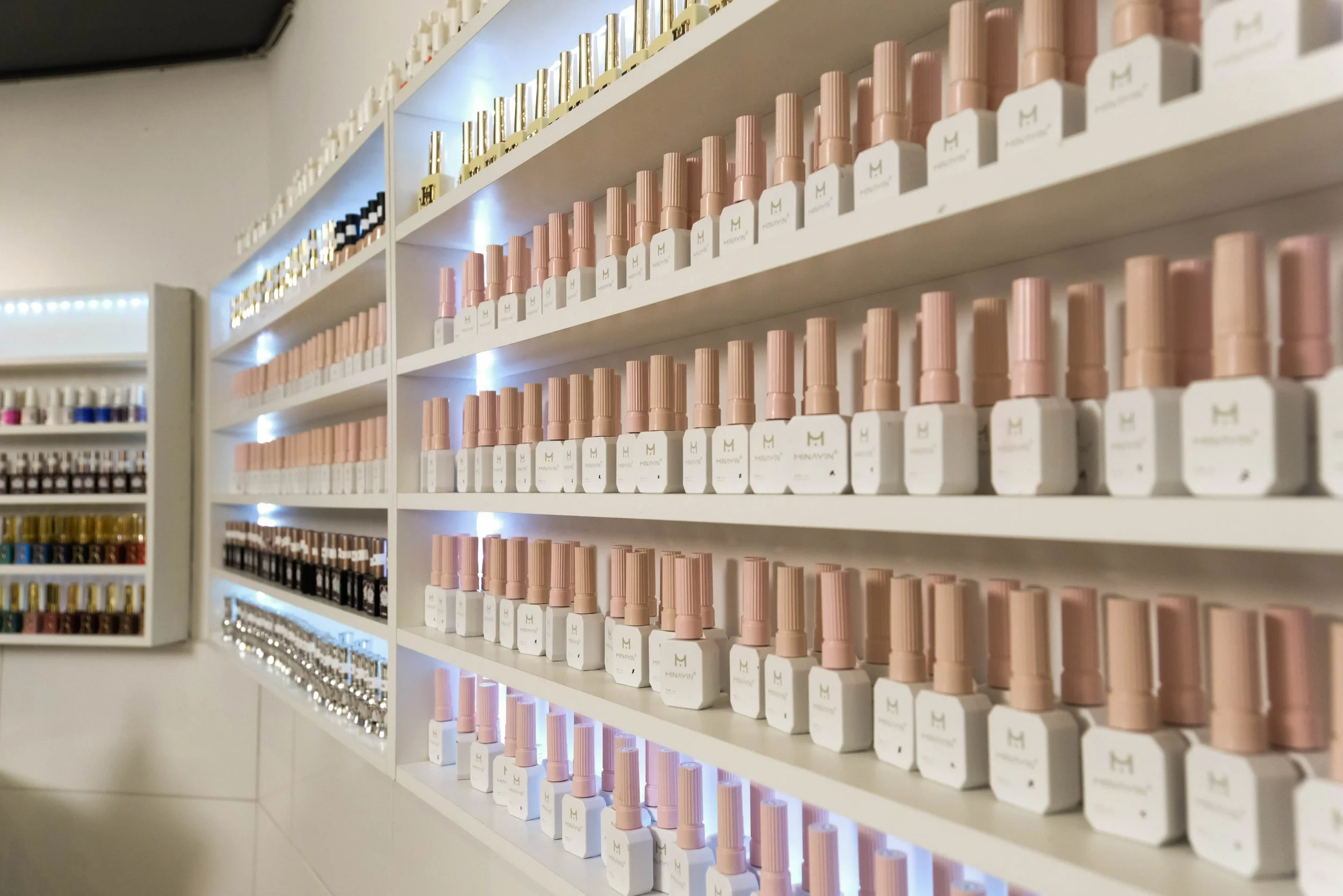 Schrankregale mit Nagellackflaschen in verschiedenen Farben und Marken. Shelves voller Nagellackflaschen, hauptsächlich in rosa, weiß und gold.