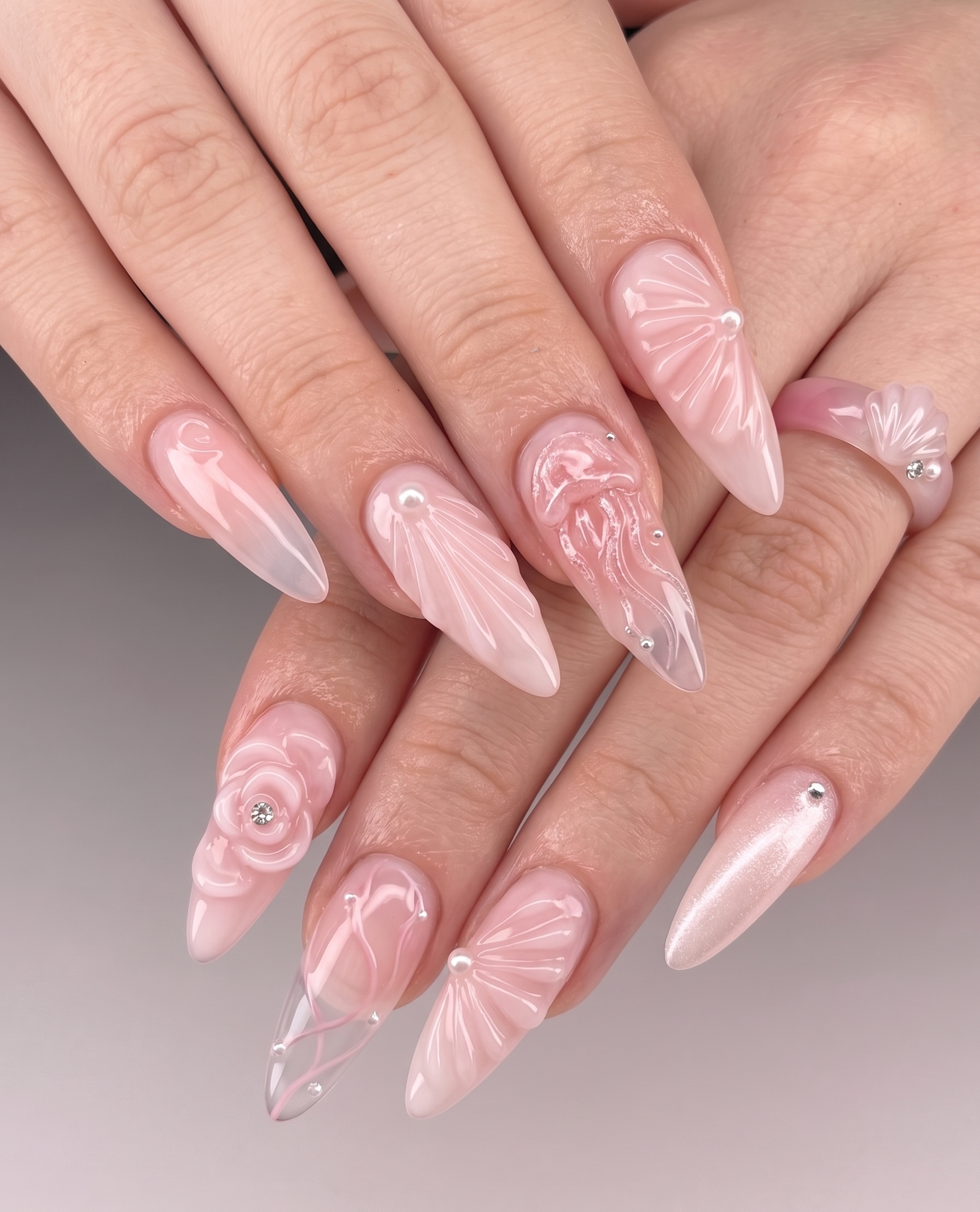 Nahaufnahme von langen, spitzen, blassrosa Kunstnägel mit weißen Linien und kleinen Schmucksteinen. Hand mit lackierten Fingernägeln.