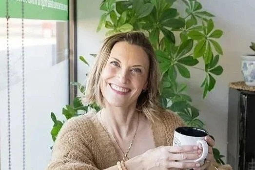 Woman smiling and holding a mug in a room with green plants.