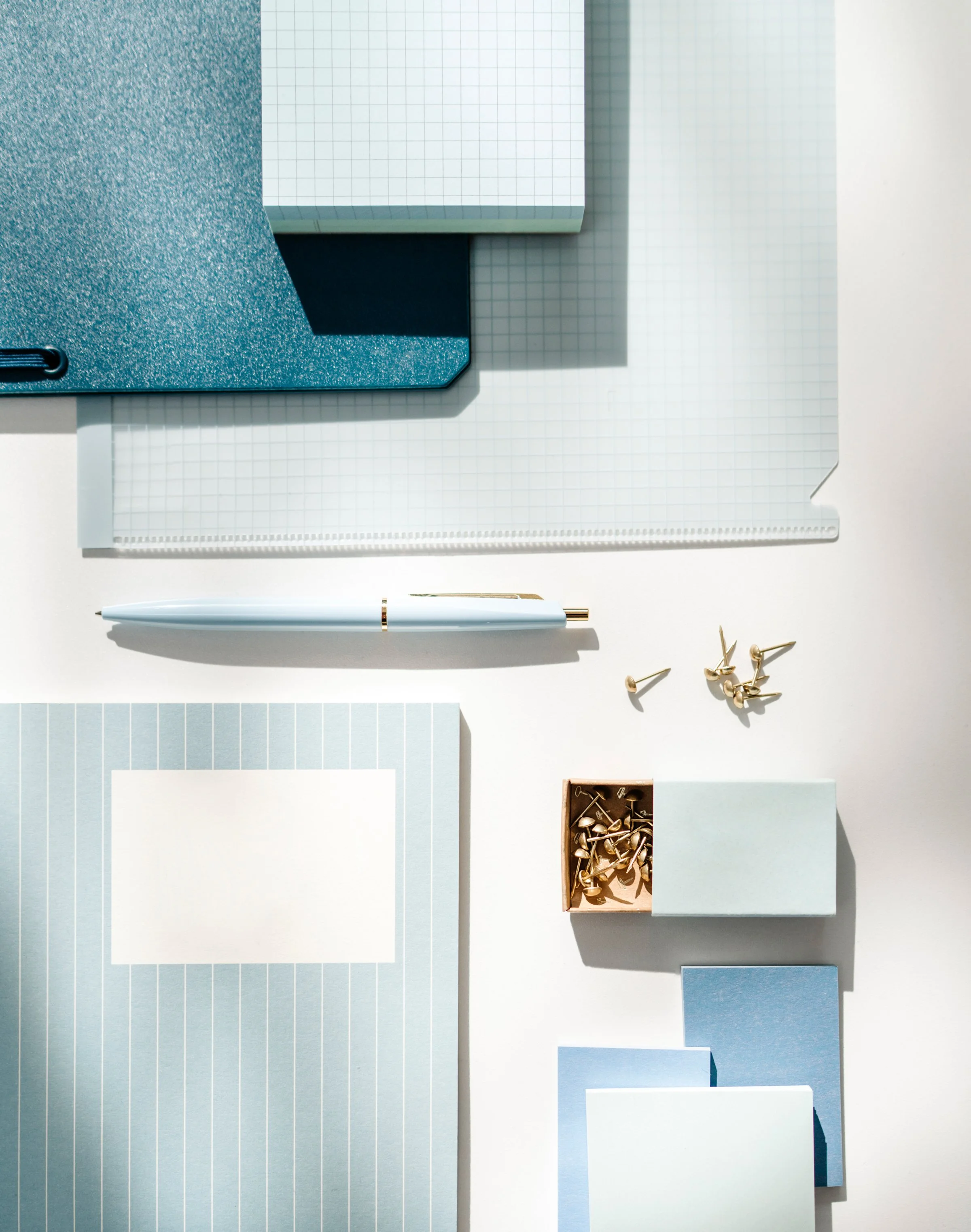 Flat lay of notebooks, notepads, a pen, paper clips, and small cards in various shades of blue and white.