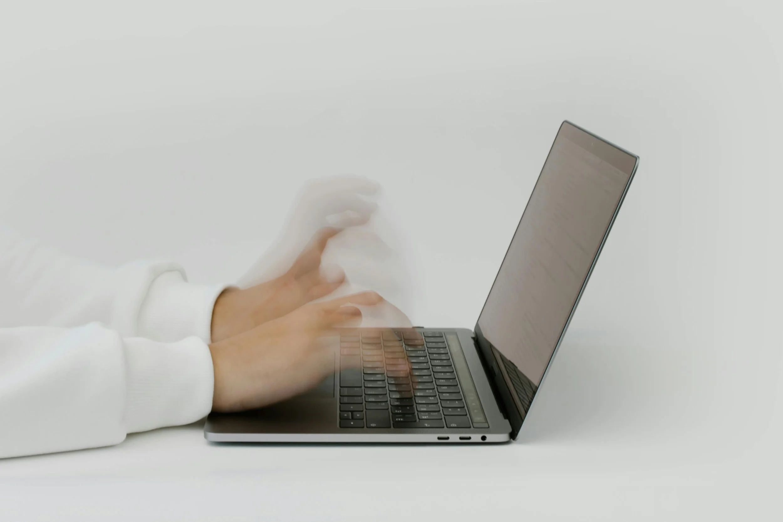 A person wearing a white long-sleeve shirt typing on a laptop with a blurred motion effect.