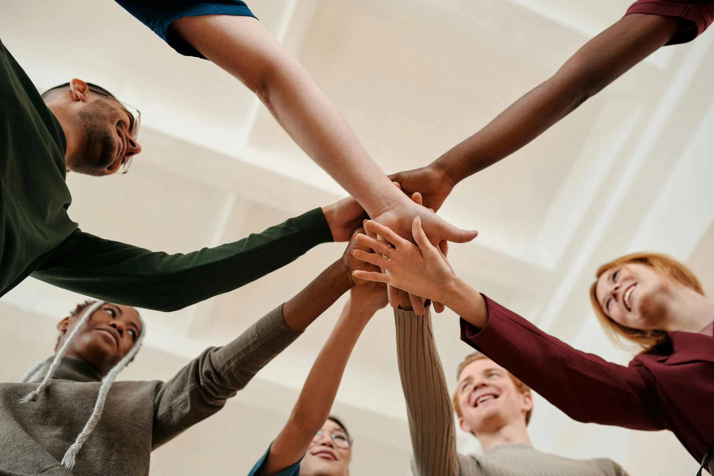 Group of diverse people working together, stacking hands in a gesture of teamwork and unity indoors.