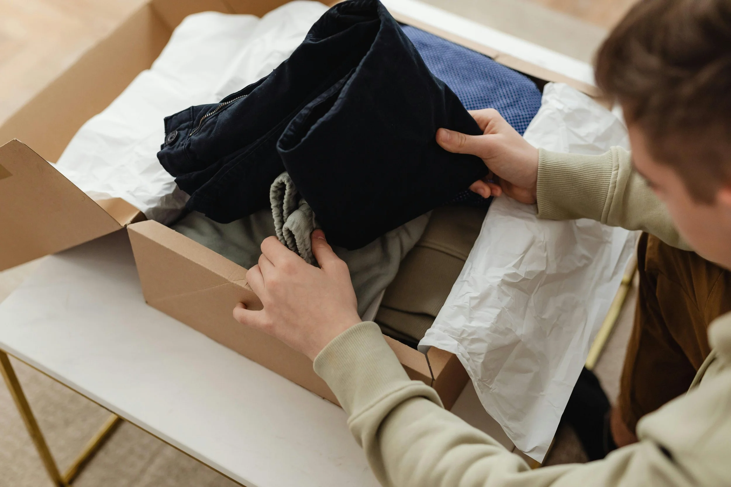 Person packing casual clothes into a cardboard box