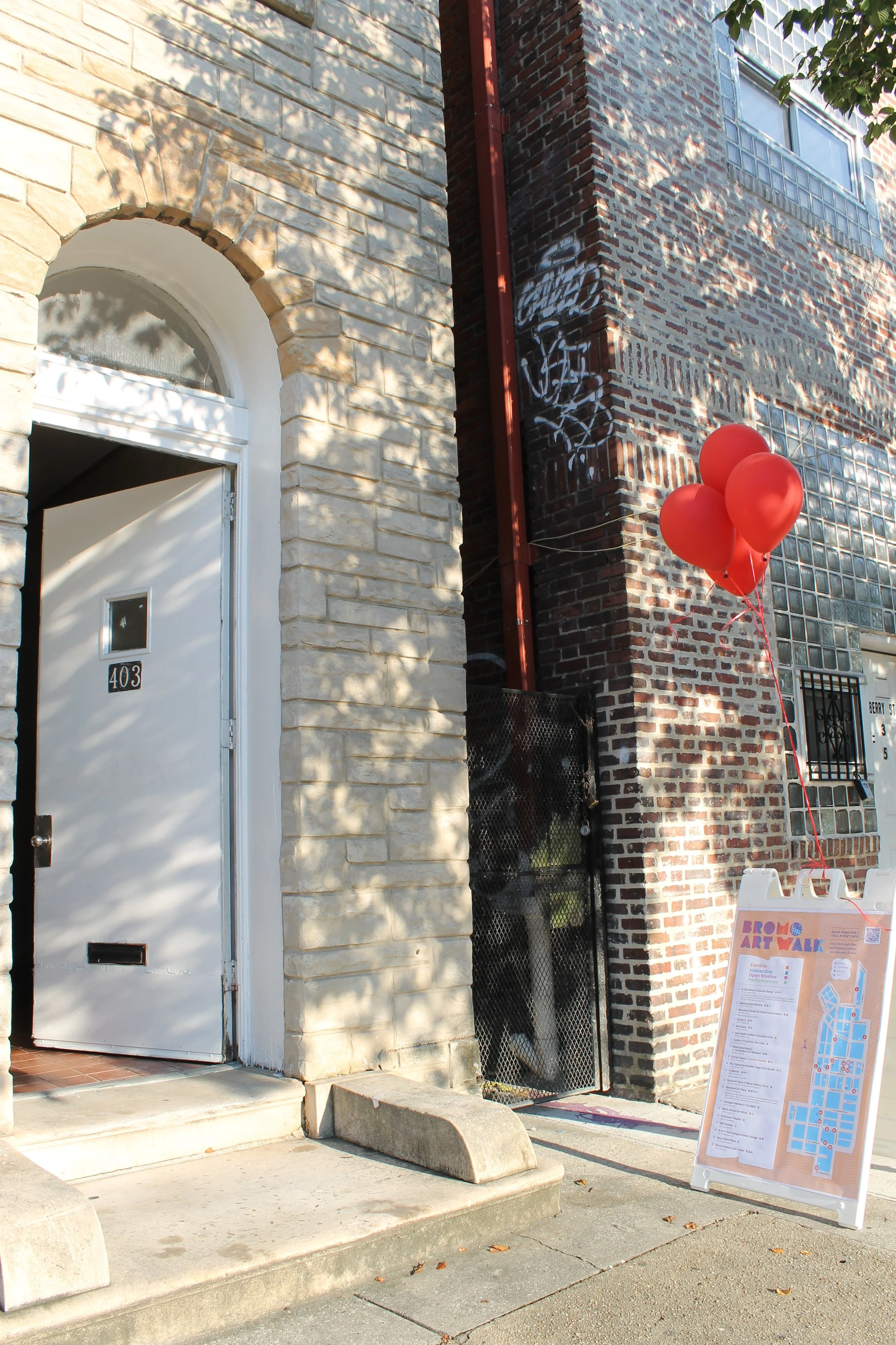 Red balloons tied to a signboard in front of a brick building with a white door and a sidewalk