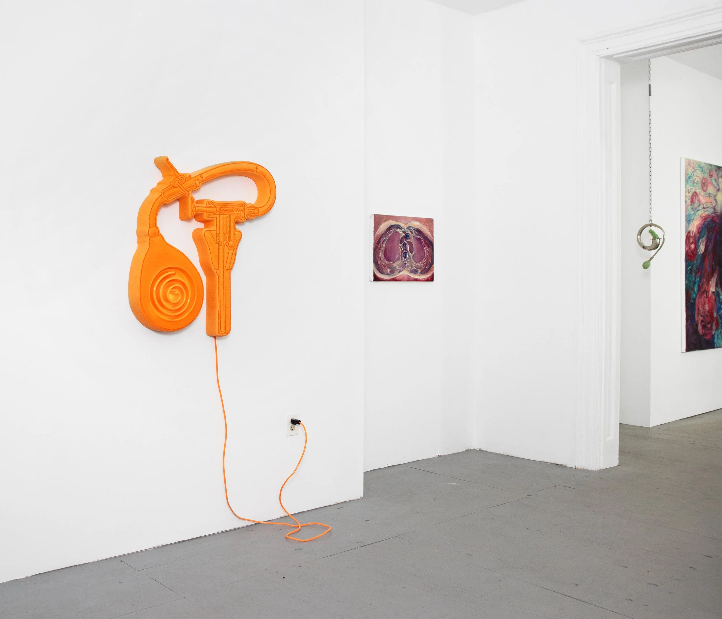 Orange Wall Art piece resembling a hand-held grenade launcher with a cord hanging down on a white gallery wall.