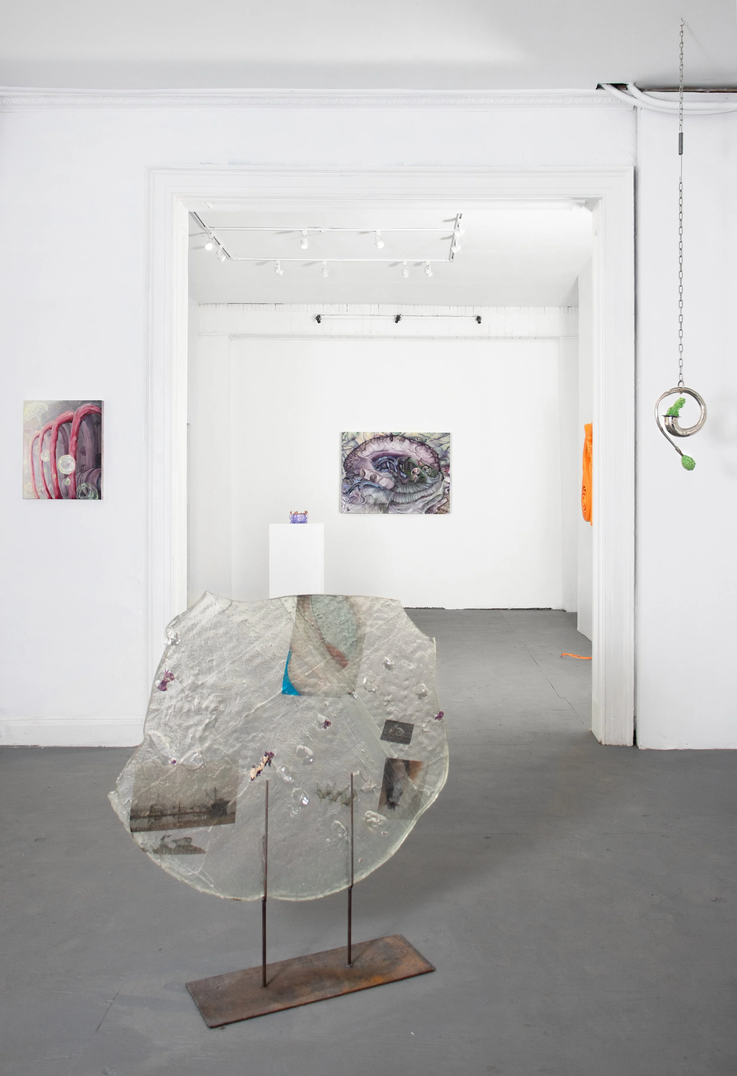 An art gallery with abstract paintings on white walls and a mixed media sculpture in the foreground on a gray floor.