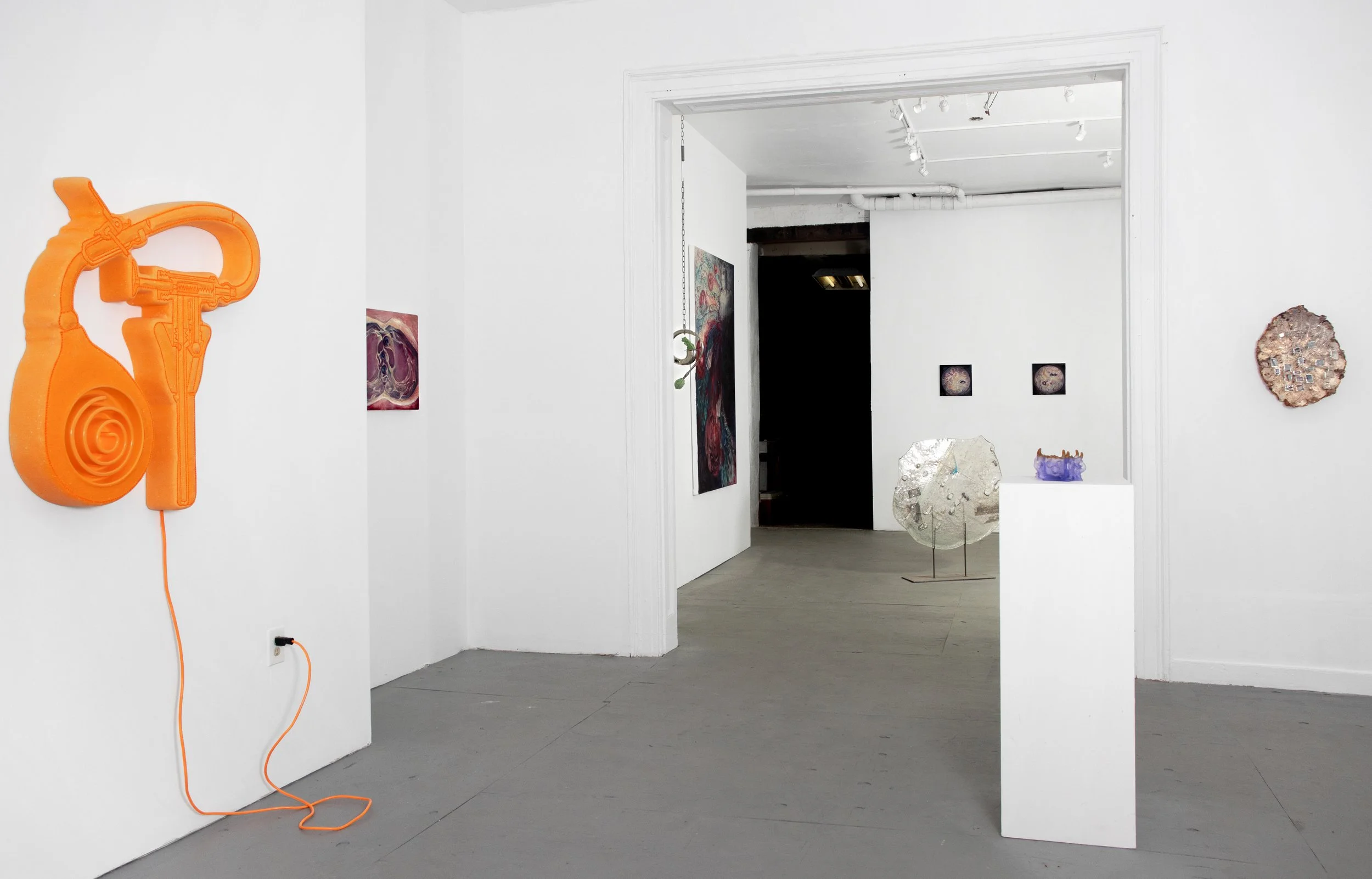 Art gallery with white walls displaying various contemporary sculptures and paintings, including an orange headphone-shaped sculpture on the left and a metallic circular sculpture in the center.