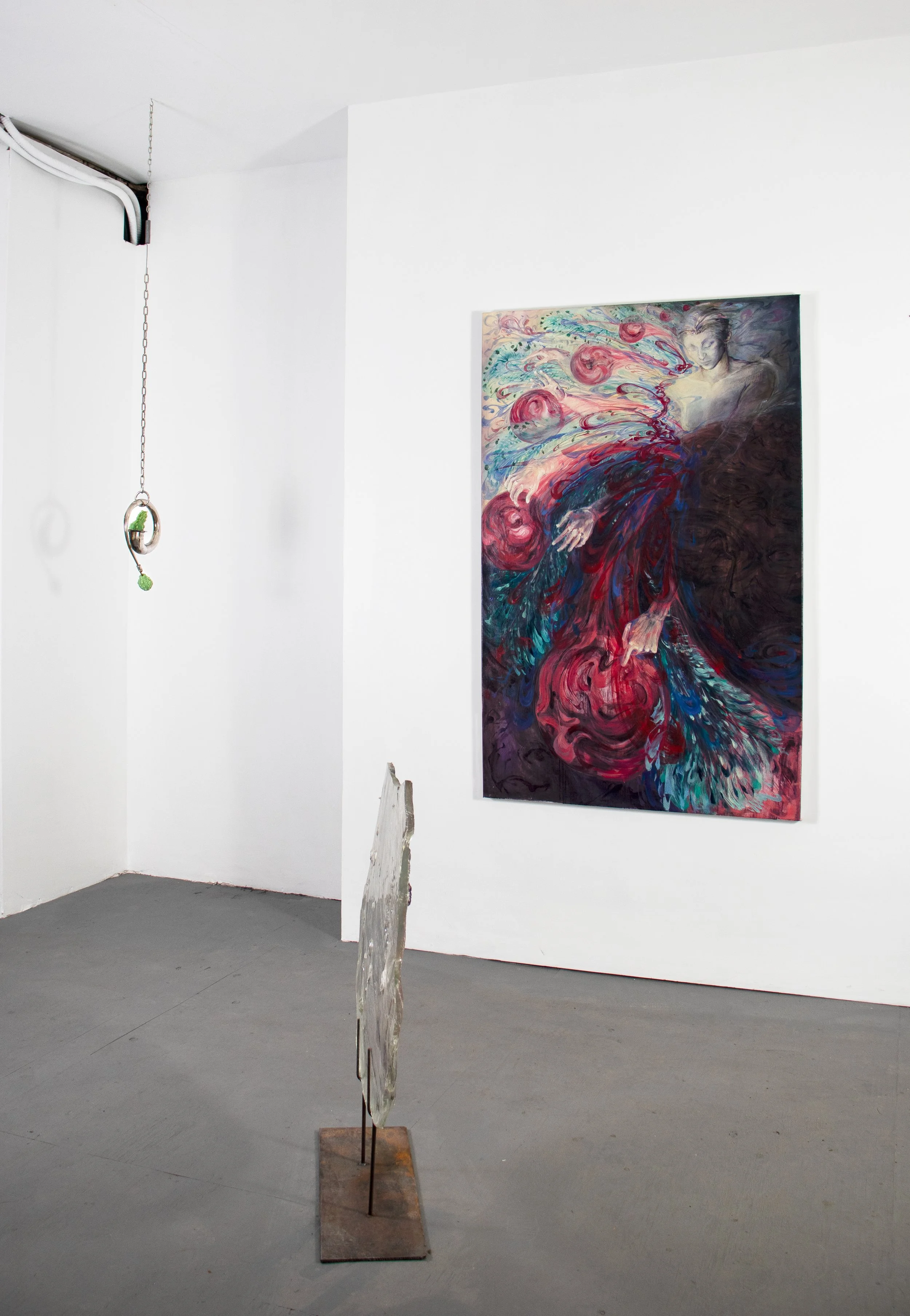 An art gallery with a large colorful painting of a woman in red and blue swirling around her on a white wall, a small sculpture on a stand in the foreground, and a hanging ring with a small green object attached to the ceiling.