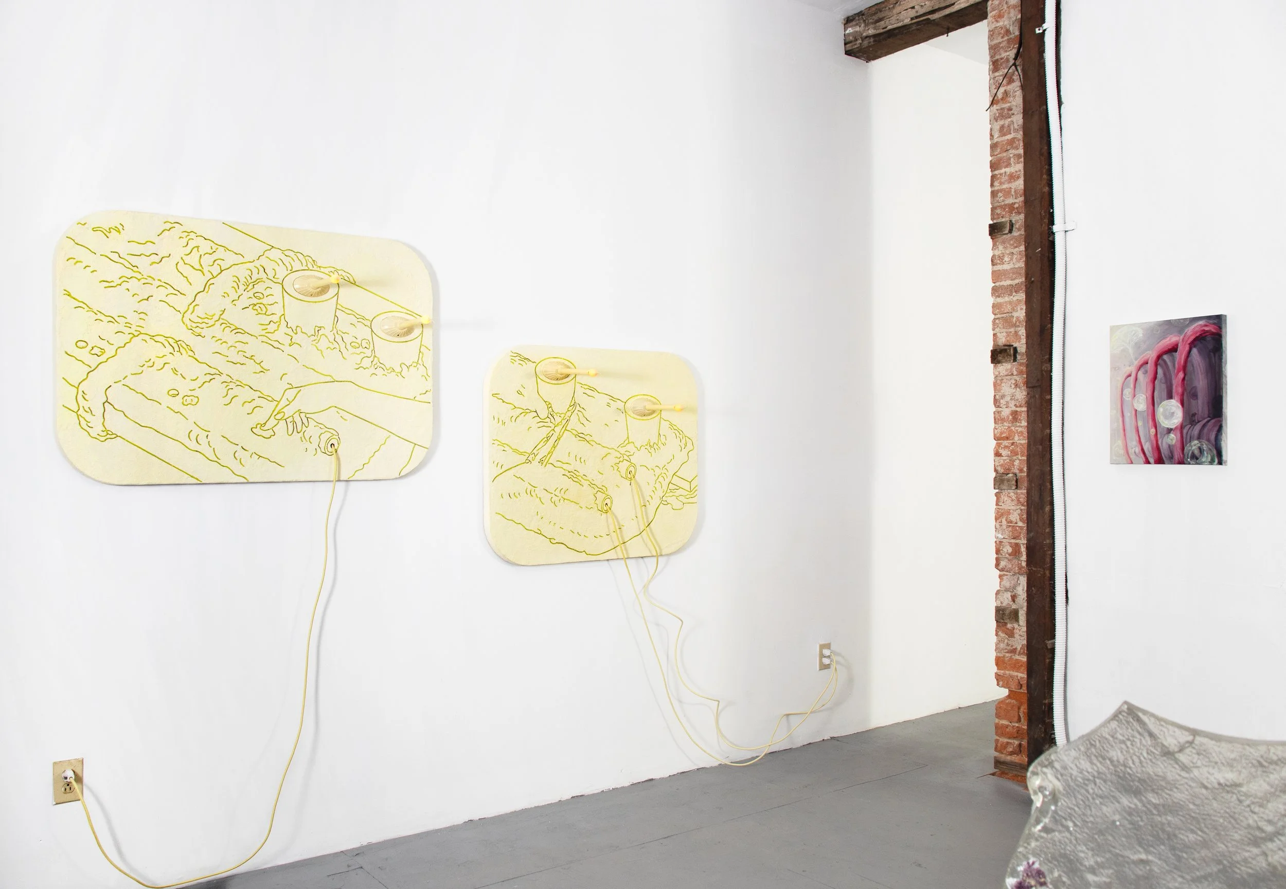 Art installation featuring two yellow background panels with abstract line drawings of hands and objects, connected by yellow wires, on a white gallery wall. A smaller painting with pink and purple hues is visible on the right.