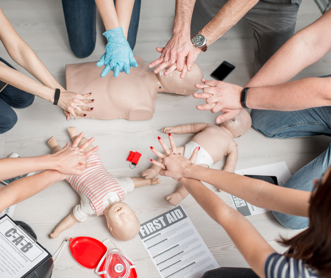 Group of people practicing CPR on mannequins during a first aid training session, with first aid instructions and equipment on the floor.