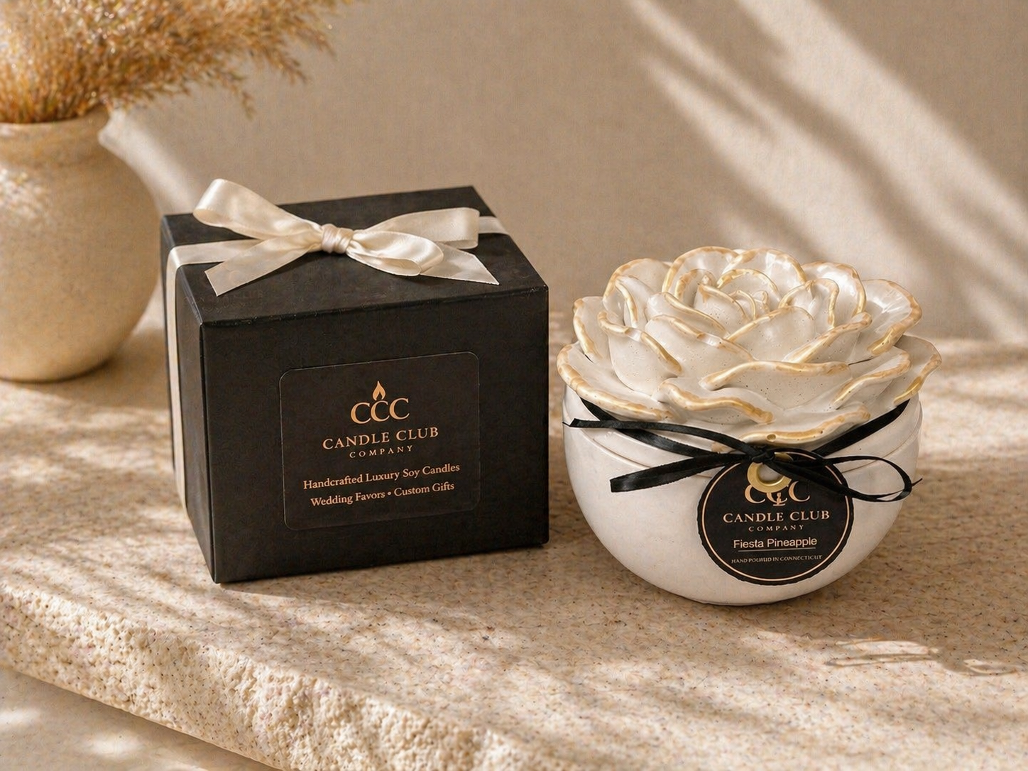 Luxury floral vessel candle displayed next to black gift box on elegant neutral background with natural light.