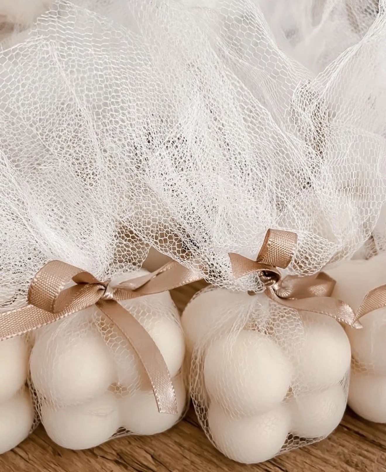 A close-up of a gift wrapped with white netting and tied with a light pink satin ribbon, containing white eggs.