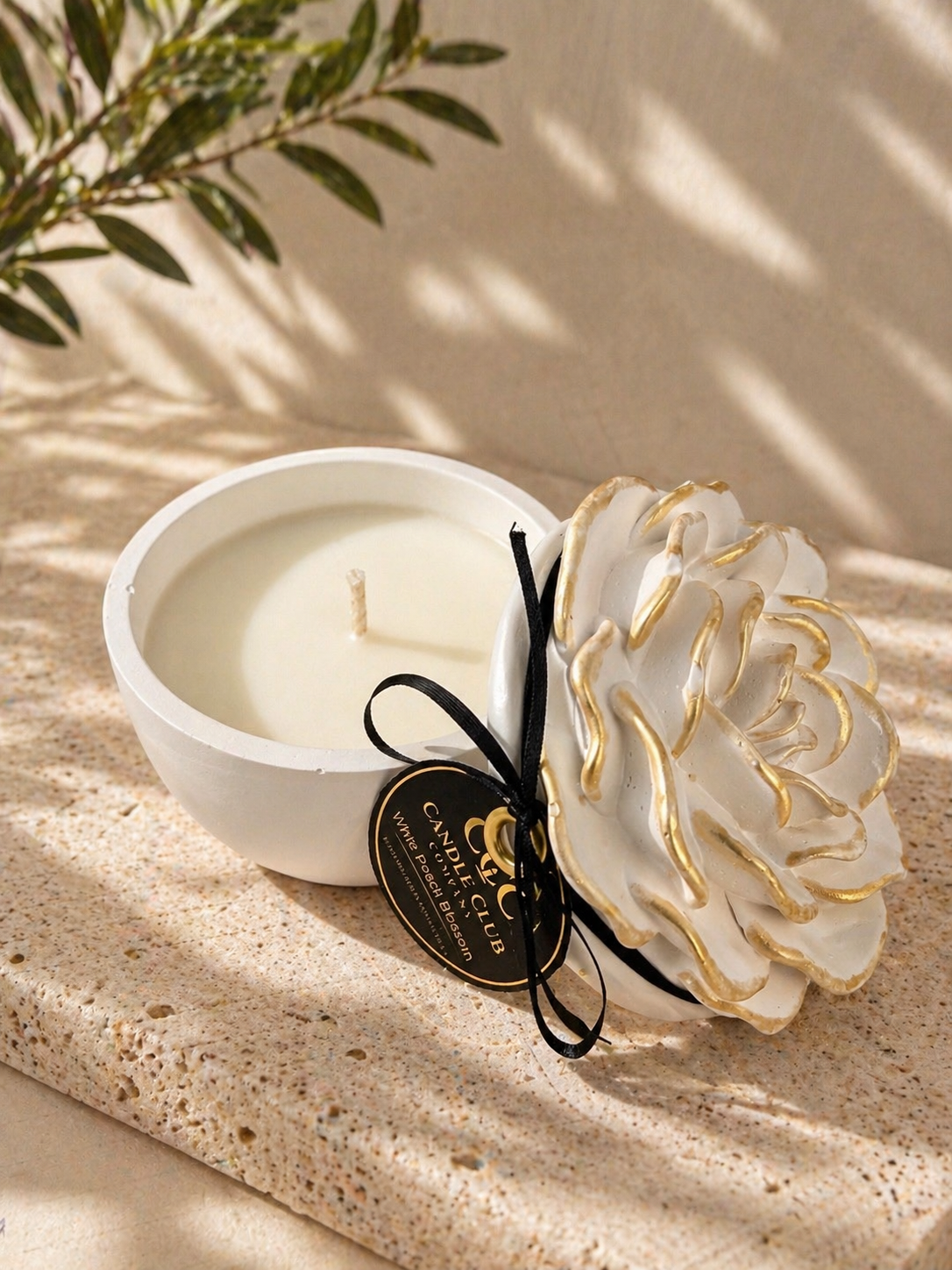 Open decorative soy candle with sculpted flower lid beside reusable vessel on warm neutral background.