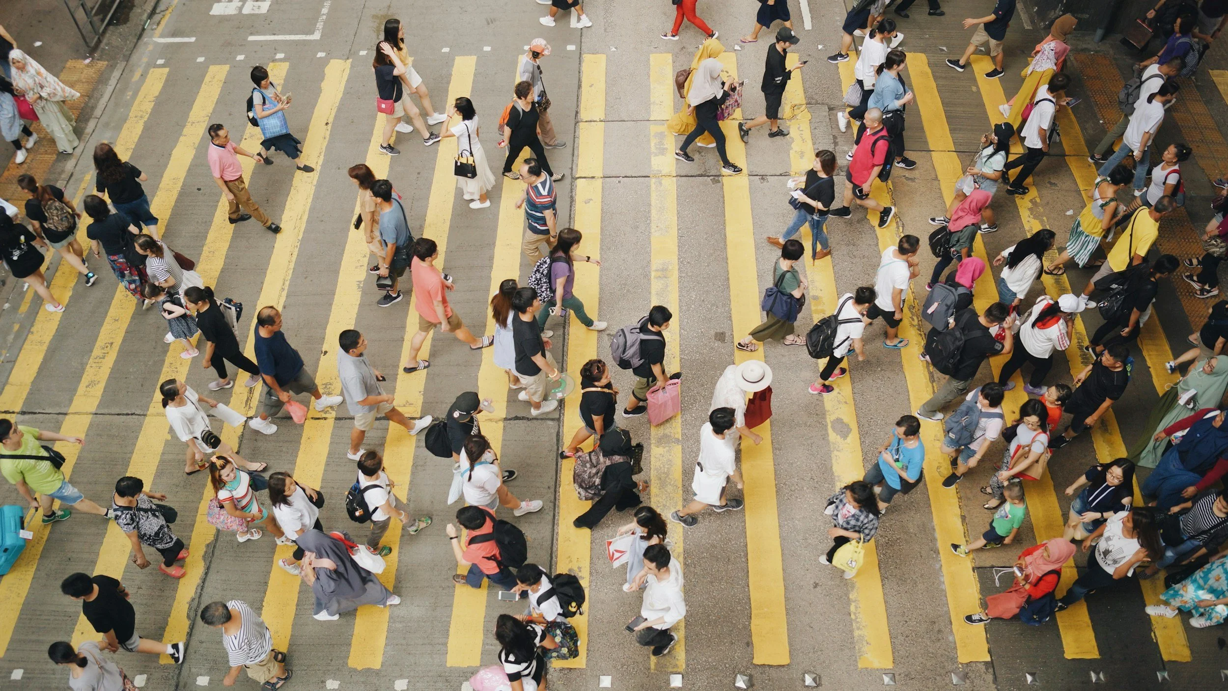 Crowd of pedestrians crossing a street at a crosswalk with yellow lines, seen from above in Hong Kong.