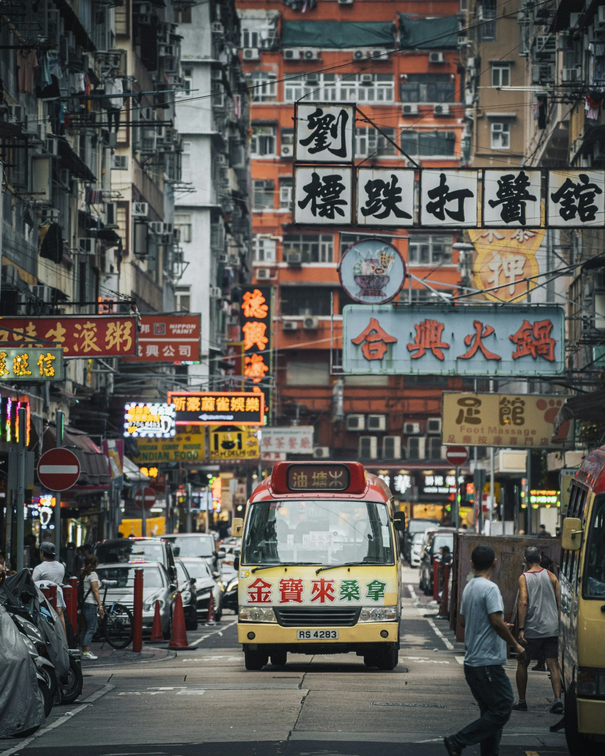 A busy street scene in an Asian city with neon signs and a small bus in the center.