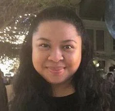 A person standing in a grassy field looking toward distant mountains with cloudy sky.