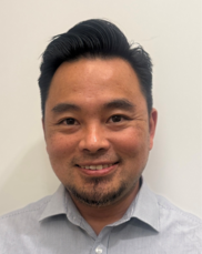 Person in a blue jacket walking through a golden grassy field with mountains in the background under cloudy sky.