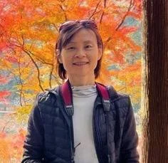 Person standing in tall grass looking towards distant mountains and clouds.