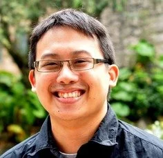 Man walking through a golden grassy field toward mountains in the distance under cloudy sky.