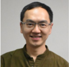 Person standing in a grassy field, facing mountains in the distance on a cloudy day.