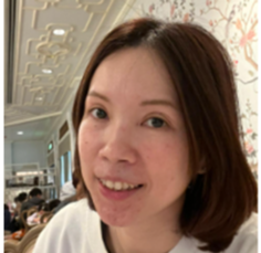Person in a blue jacket and tan pants walking through a field toward mountains with clouds in the distance.