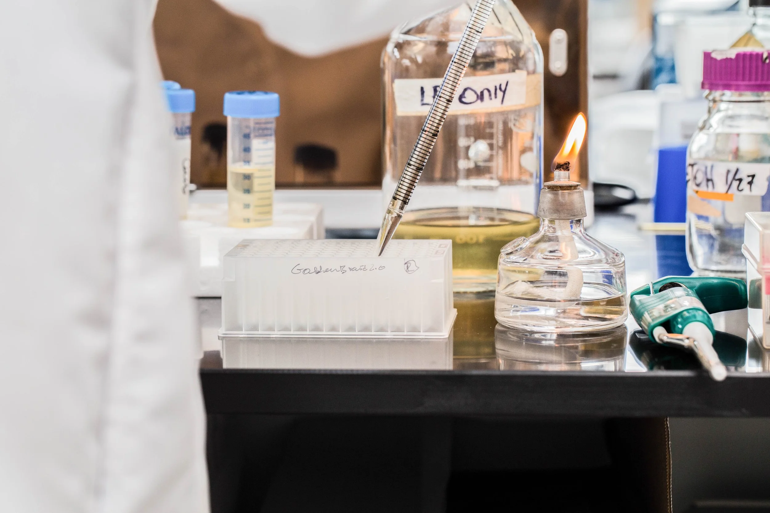 Laboratory workspace with glass containers, pipettes, a flame, and equipment for chemical experiments.